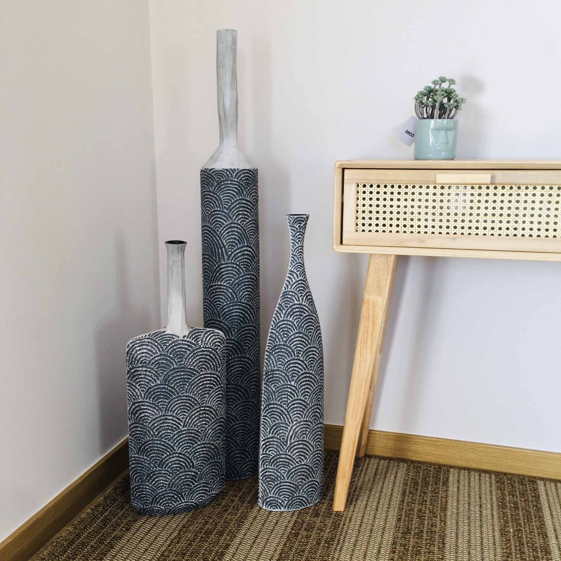 Três vasos decorativos altos com padrão azul e branco junto a uma mesinha de madeira clara com planta verde