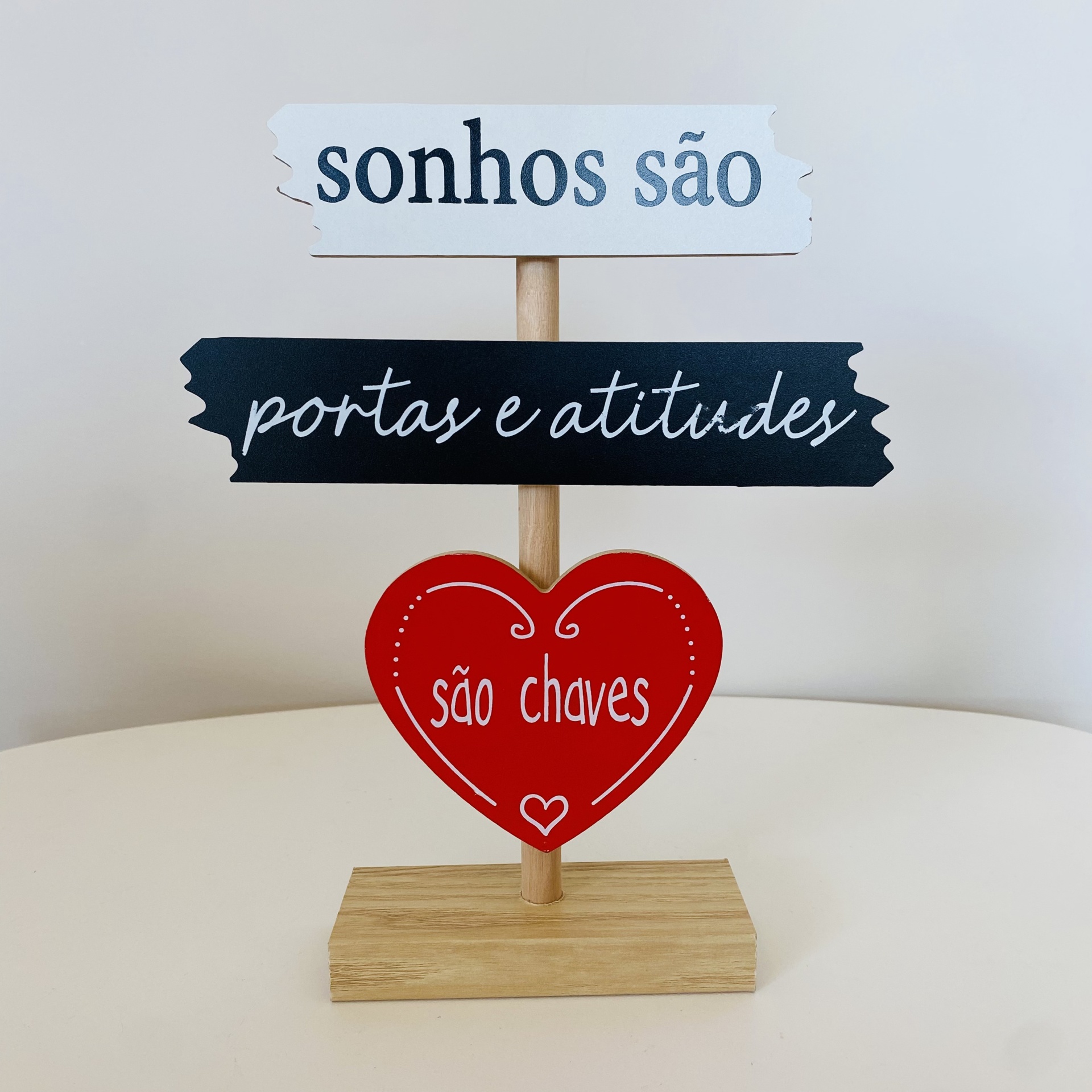 Decoração em madeira com três placas com texto em português, numa superfície branca e fundo cinzento claro