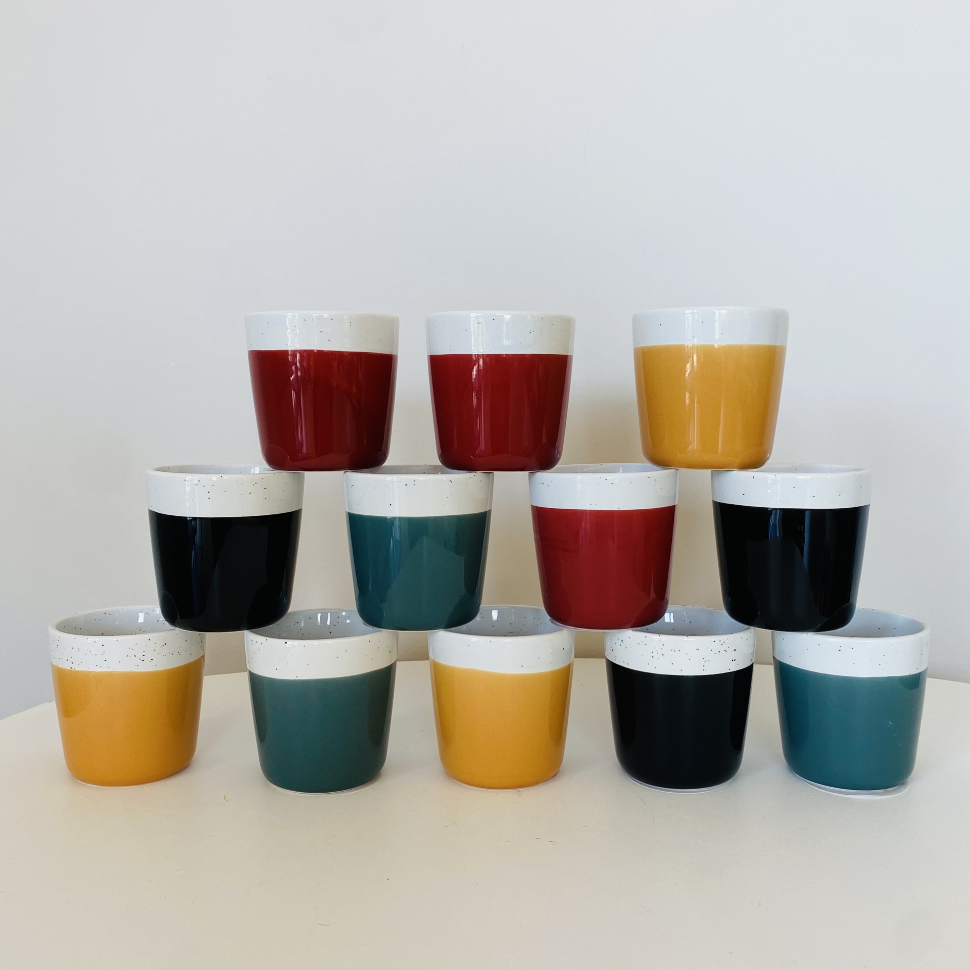 Copos pequenos de cerâmica coloridos com topo branco texturizado, organizados em pirâmide