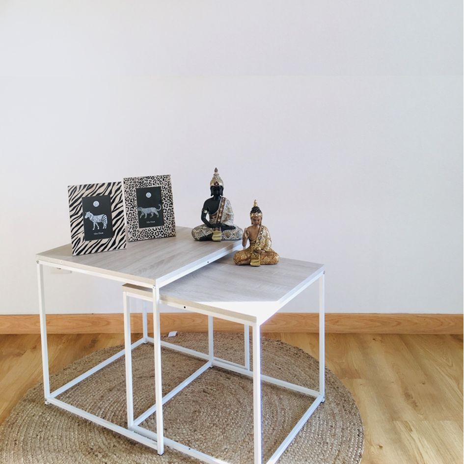 Conjunto de mesas de apoio brancas com esculturas de Buda e porta-retratos em tapete redondo.