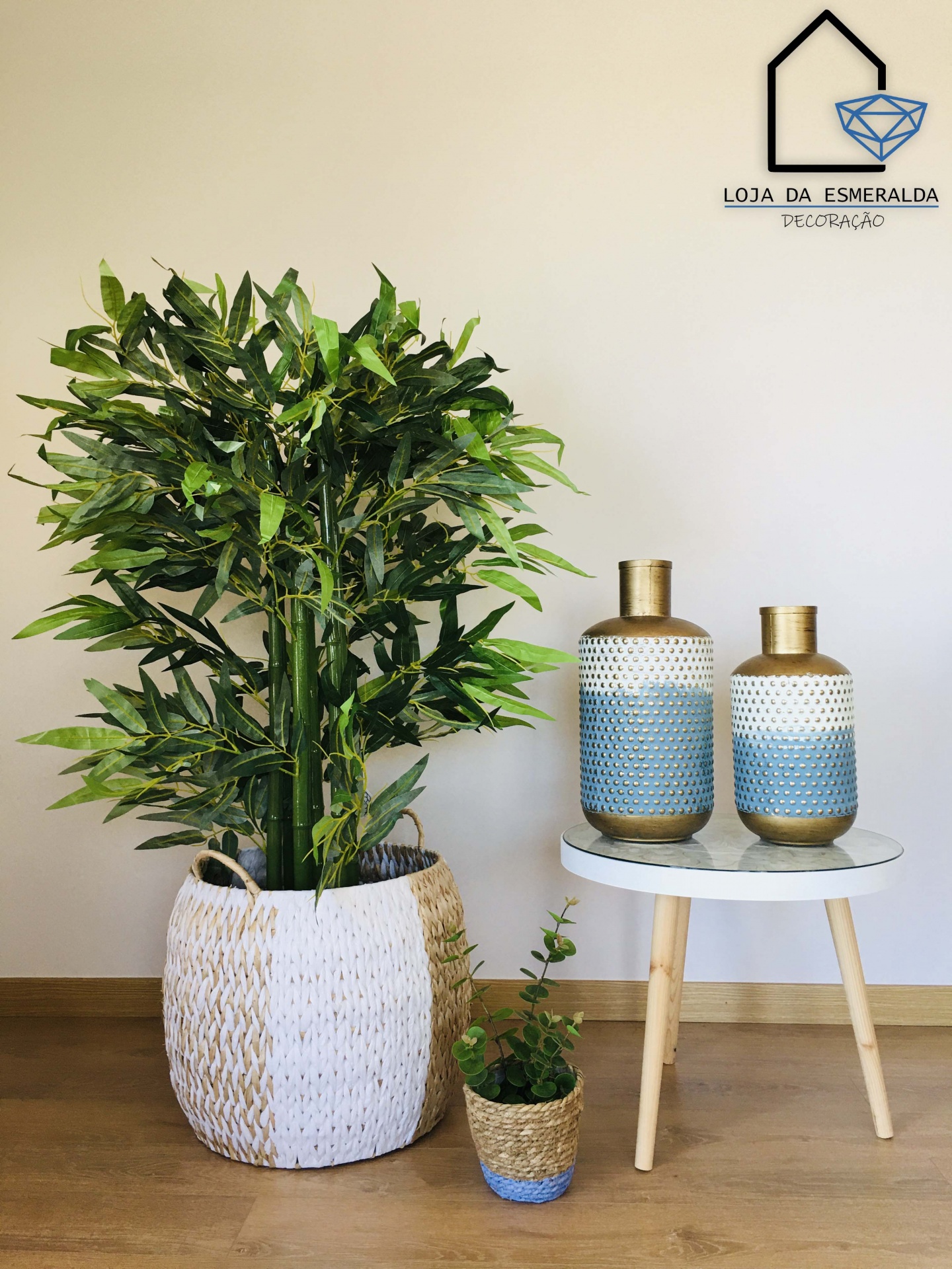 Planta artificial em cesto trançado, vasos pequenos e jarras decorativas em mesa