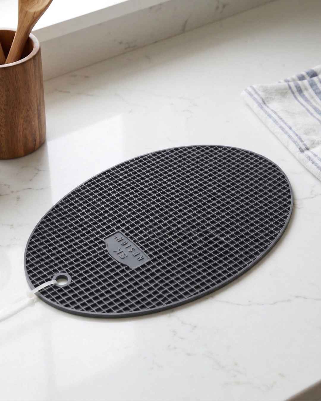 Tapete oval preto texturizado sobre bancada branca com utensílios de cozinha