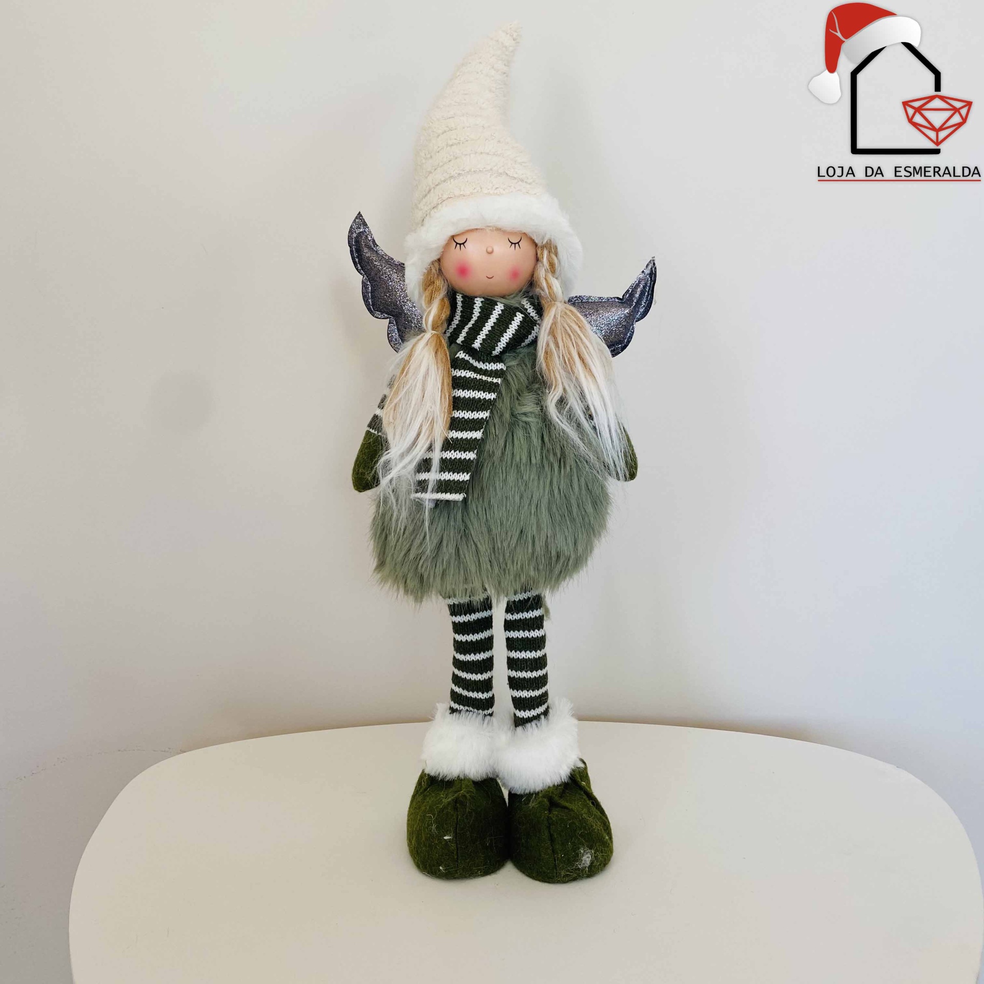 boneca decorativa com vestido verde felpudo, cachecol e collants listrados, chapéu branco pontudo, asas cinzentas, sobre superfície branca