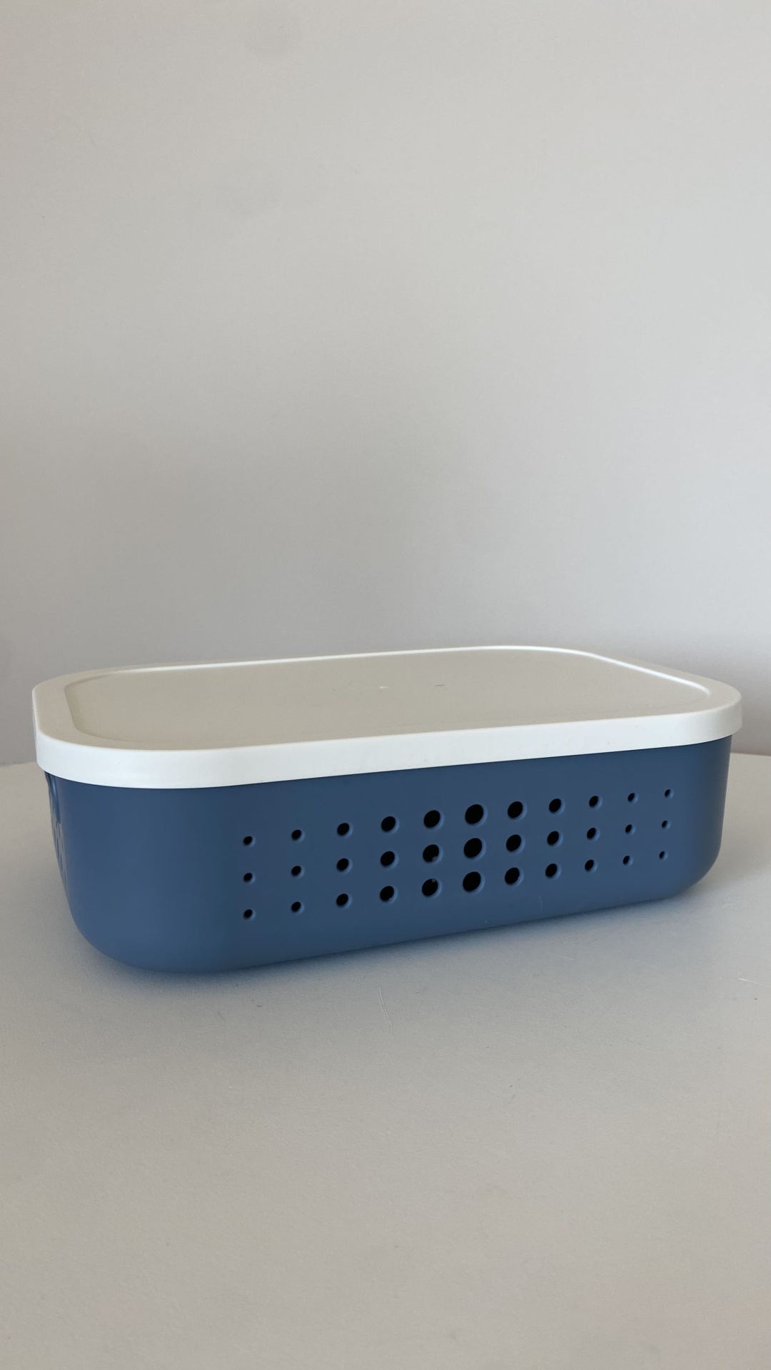 Caixa plástica azul com tampa branca e furos laterais sobre superfície cinza.