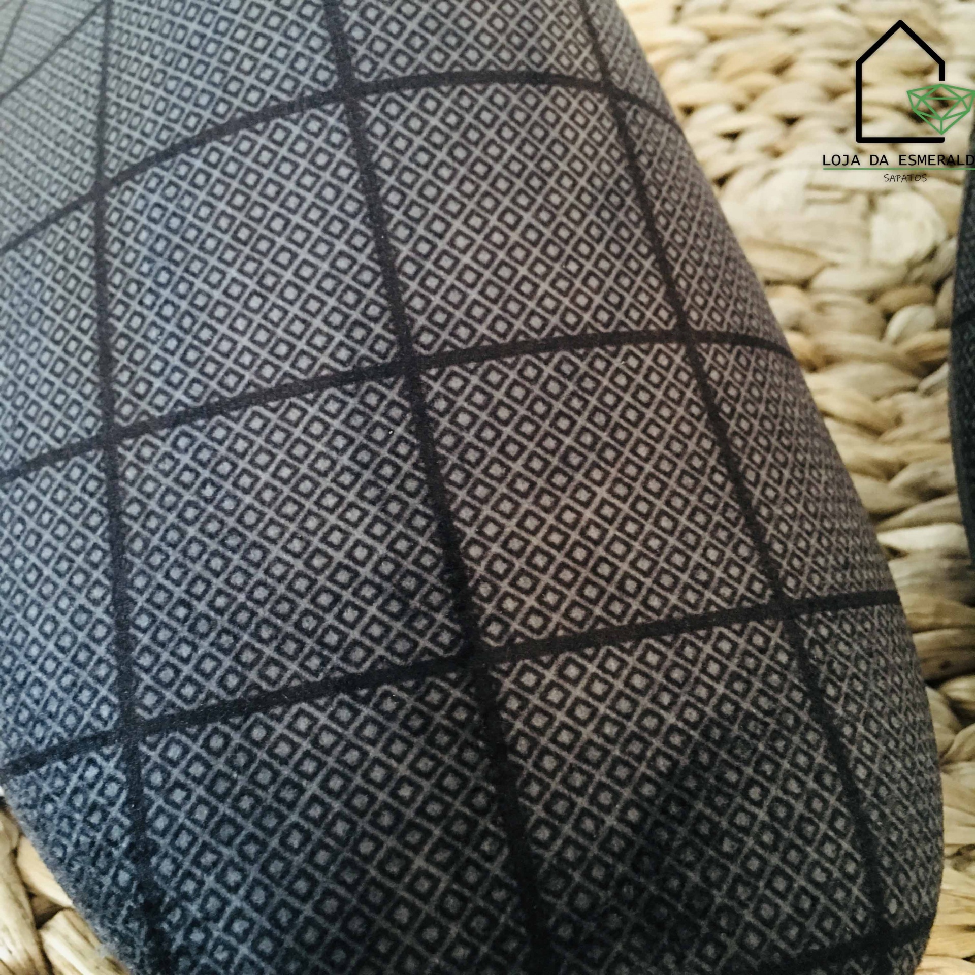 Tecido com padrão quadriculado de losangos em preto e cinza sobre superfície trançada bege