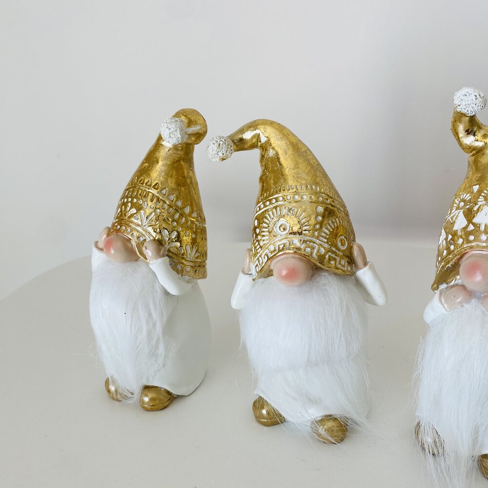 Três figuras de duendes com barbas brancas e chapéus dourados em fundo neutro