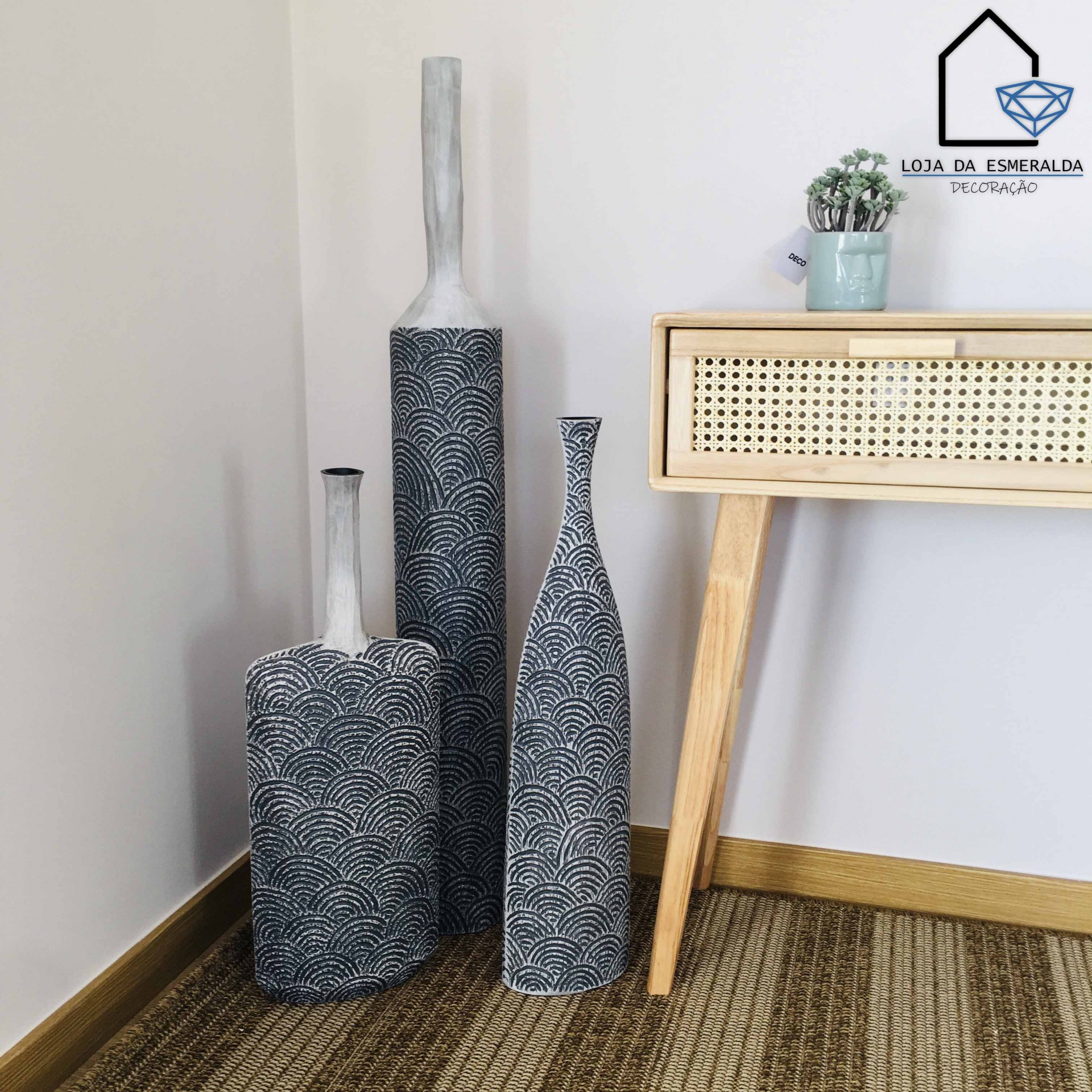 Três vasos decorativos cinza e branco ao lado de móvel de madeira clara com planta