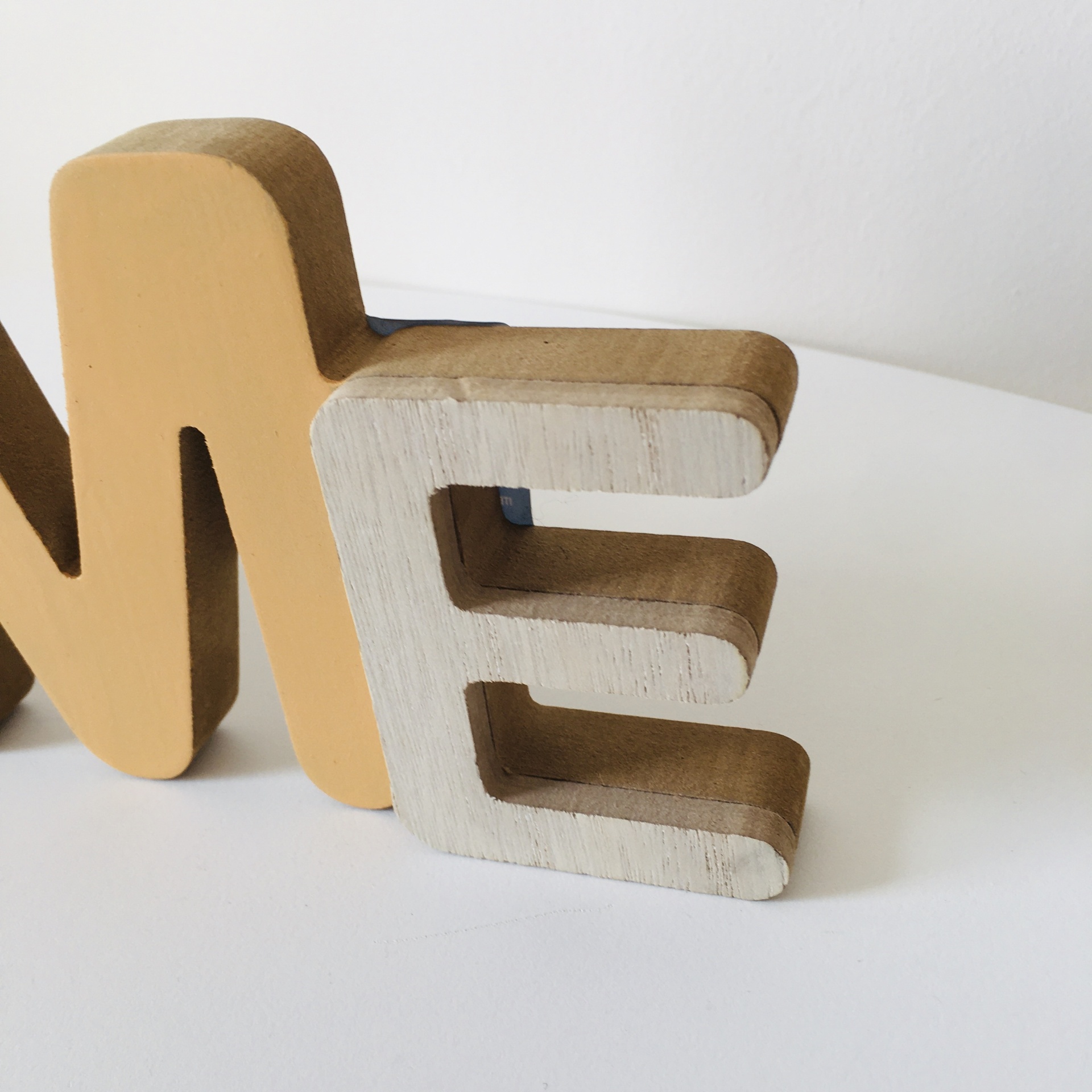 Letras decorativas de madeira pintadas 'E' branca e 'M' amarela sobre superfície branca