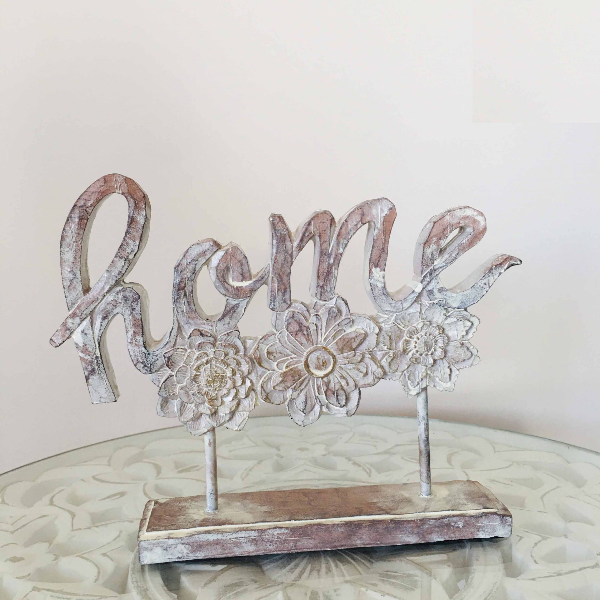 Figura decorativa branca com a palavra home e flores esculpidas sobre mesa de vidro