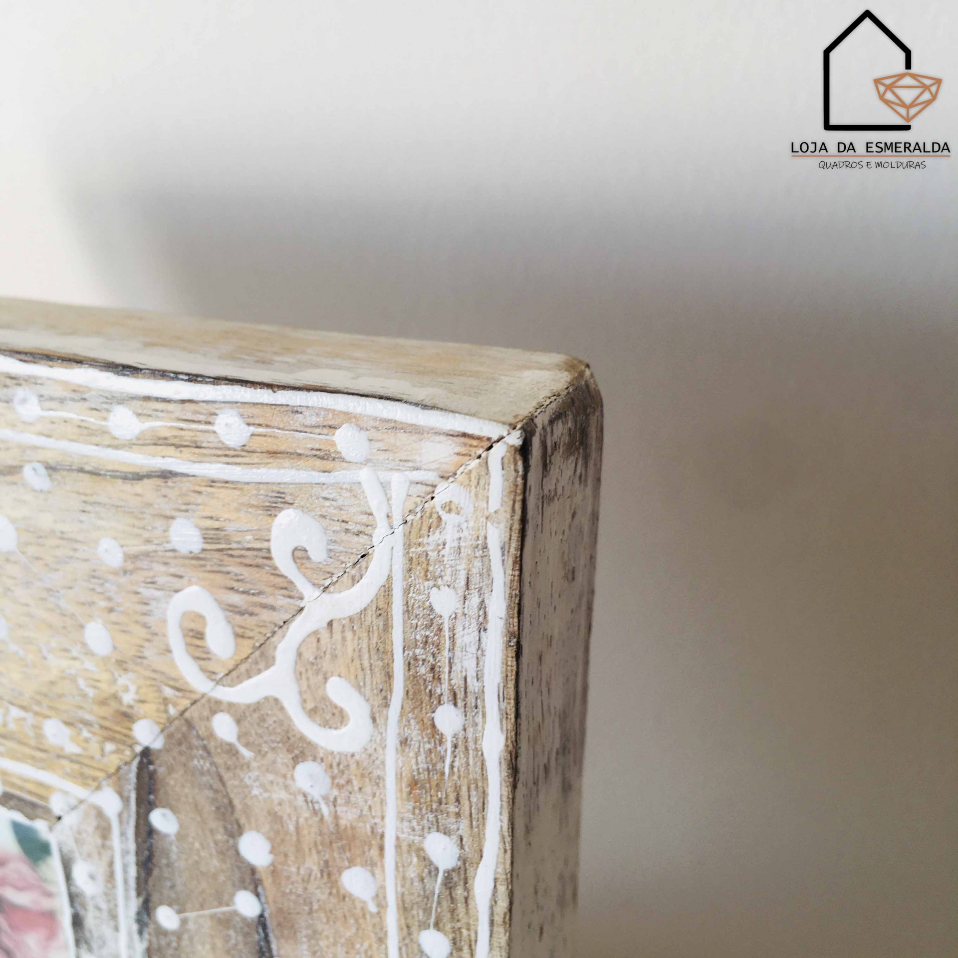 Canto rústico de moldura de madeira pintada com desenhos brancos e logotipo da loja ao fundo.