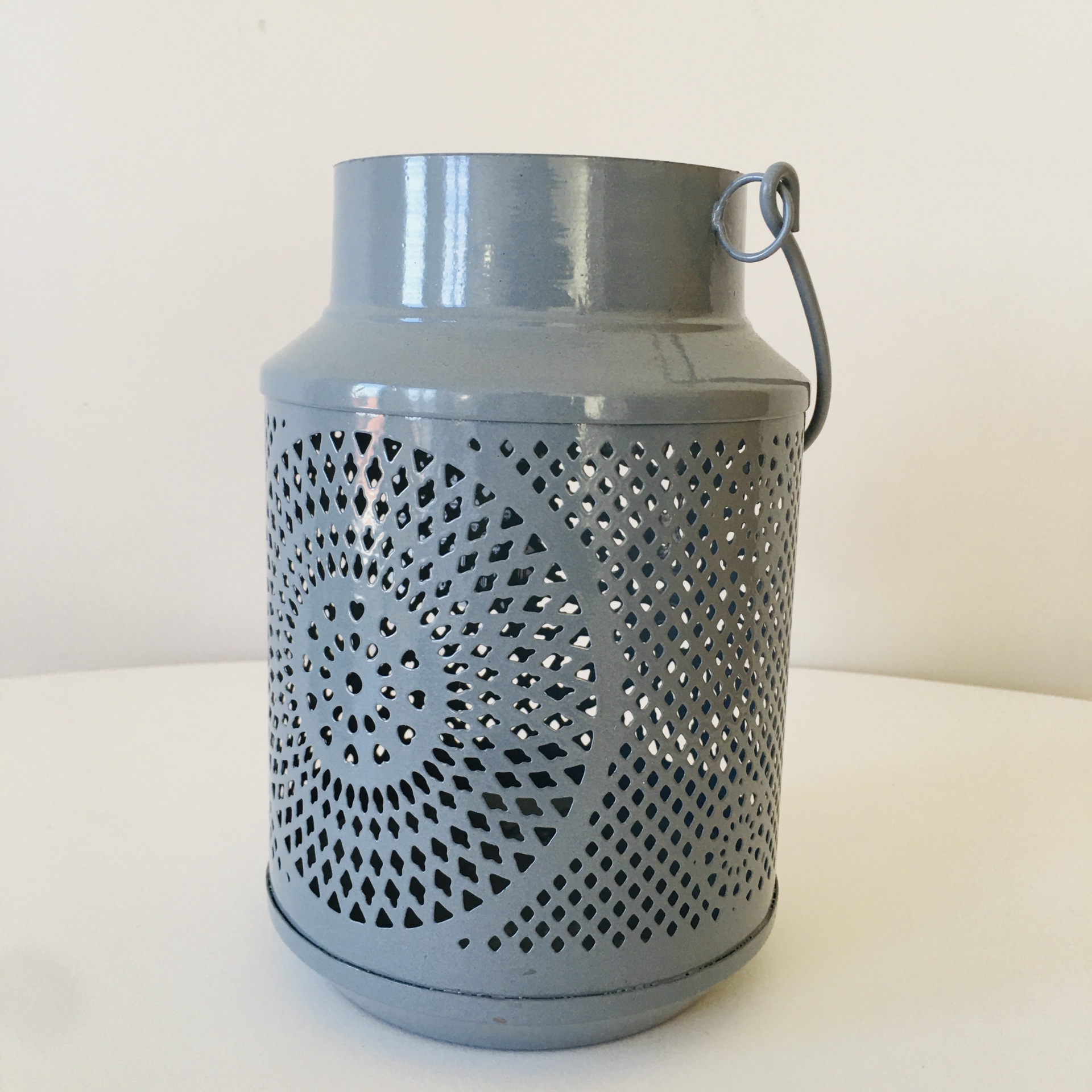Recipiente metálico cinzento com padrão circular perfurado e alça de arame