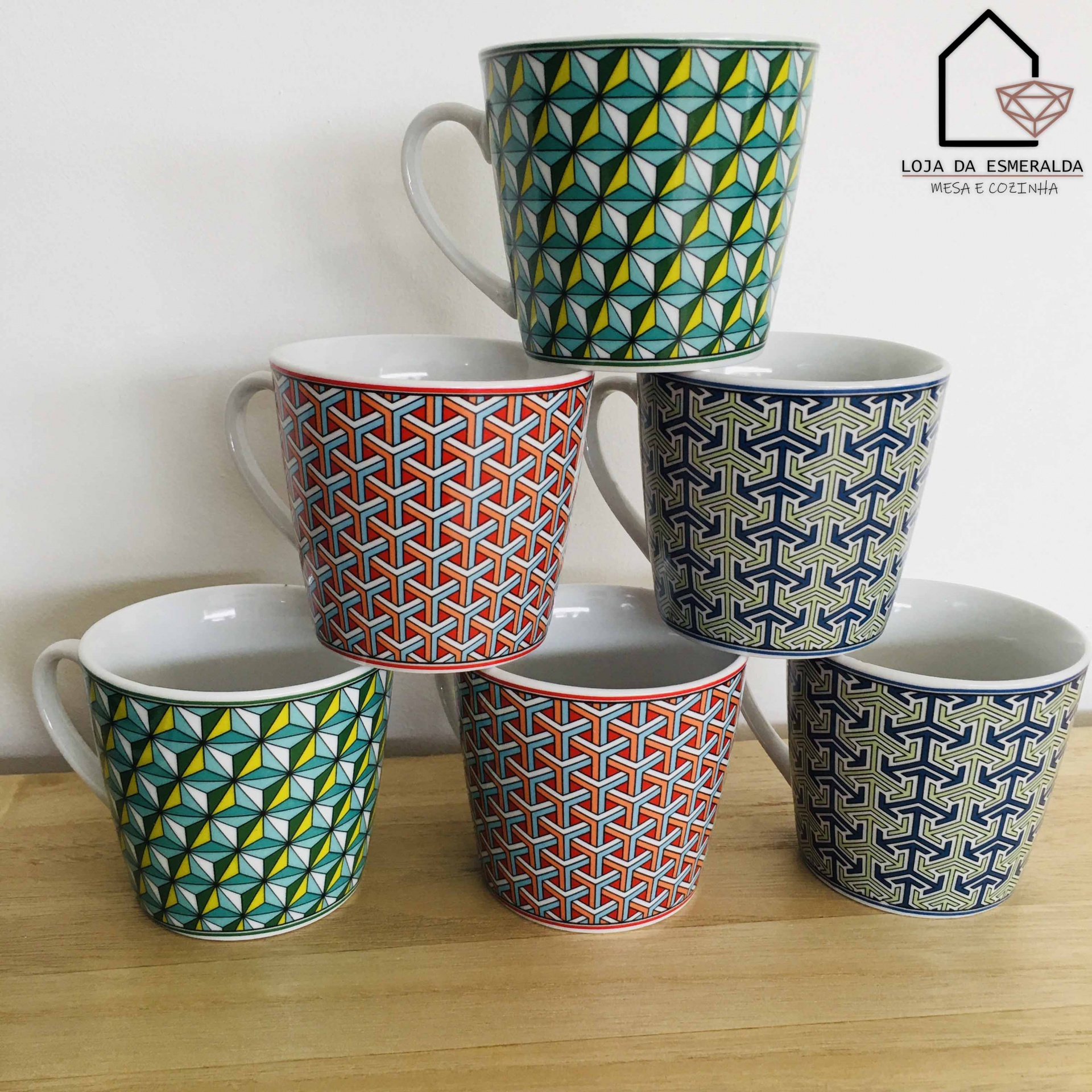 Seis canecas de cerâmica com padrões geométricos coloridos empilhadas sobre mesa de madeira