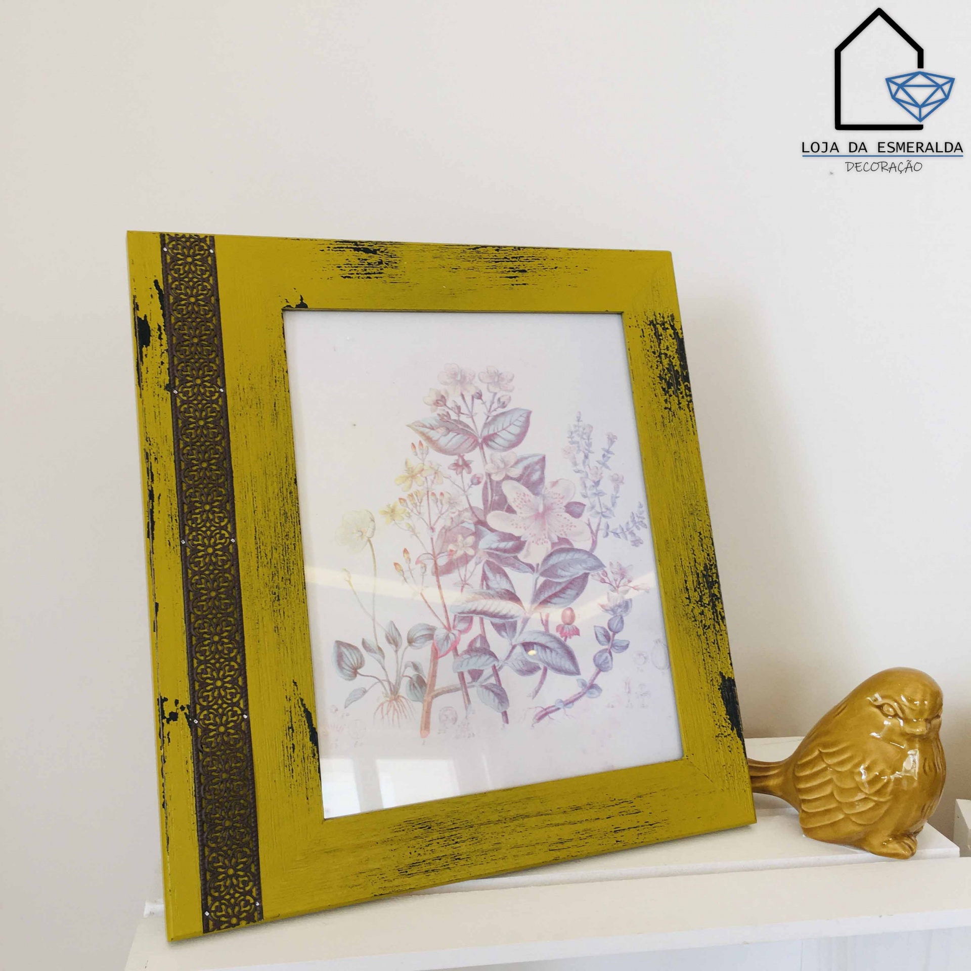 Moldura de madeira amarela com imagem floral ao lado de figura de pássaro dourado