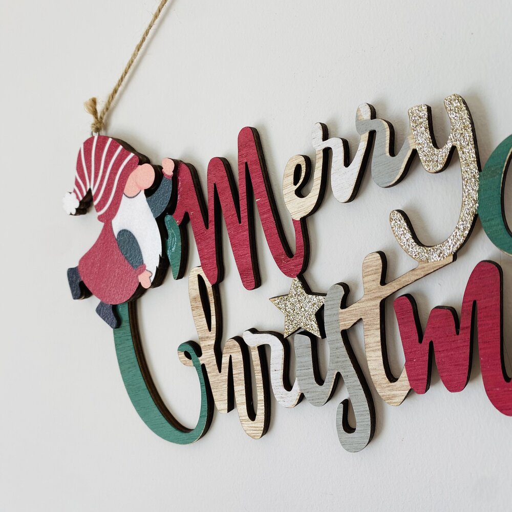 Decoração de Natal em madeira colorida com texto 'Merry Christmas' e duende pendurado.