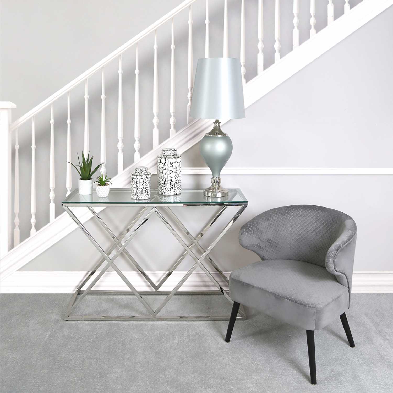 Mesa de vidro com candeeiro e velas decorativas, cadeira cinzenta de veludo, tapete cinzento e escada branca
