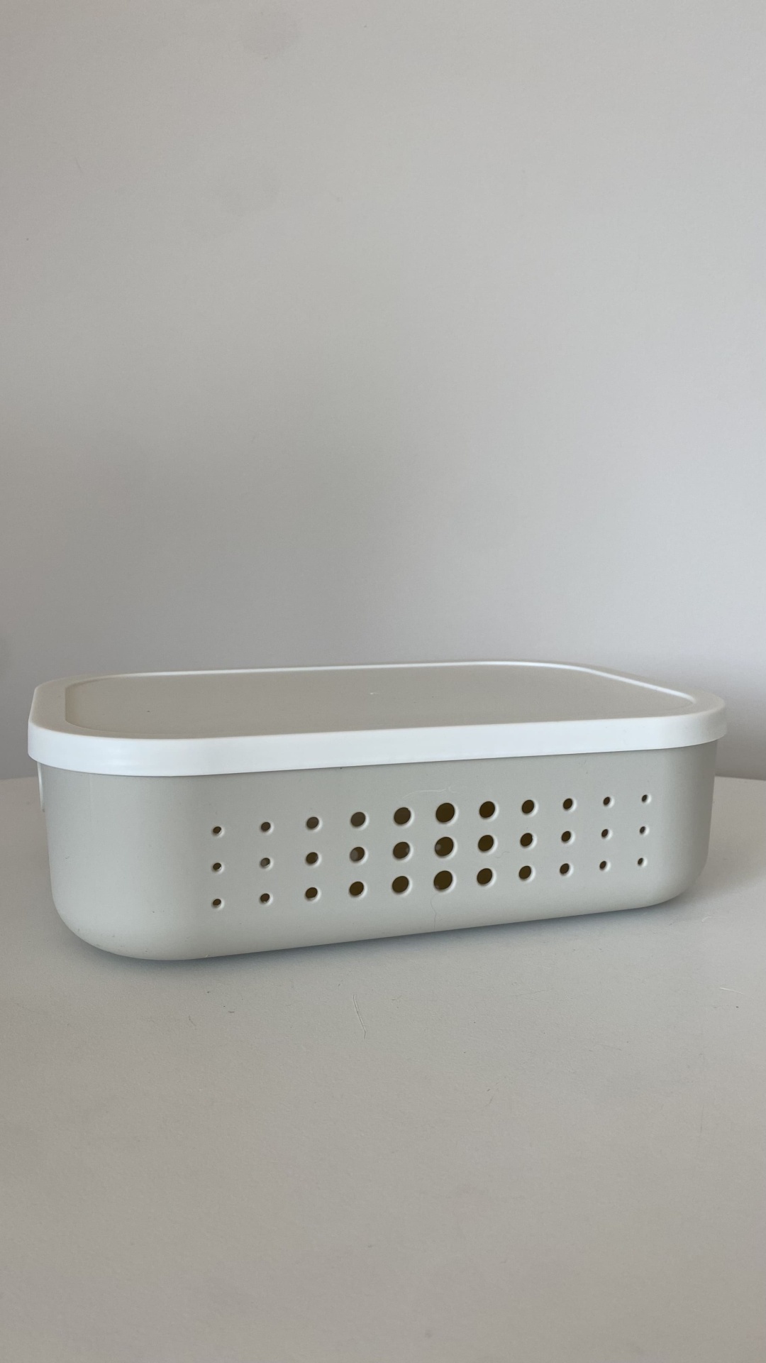 Caixa retangular de plástico cinzento com tampa branca e perfurações nas laterais