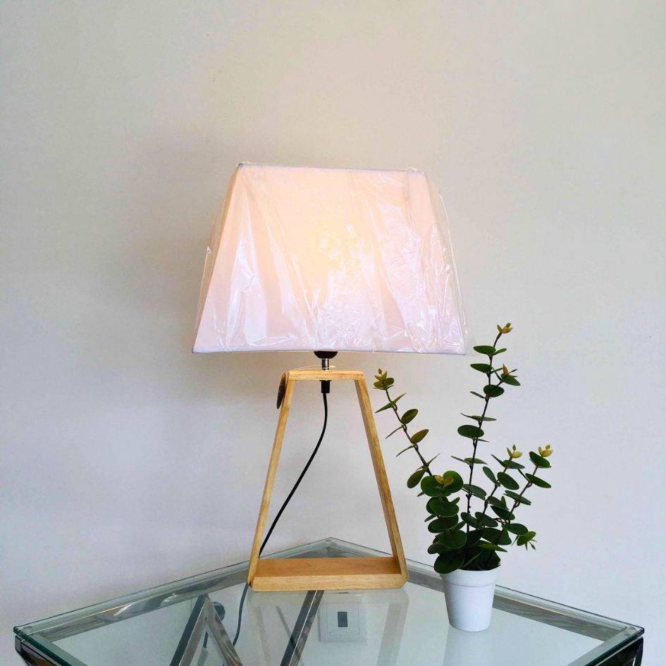 Candeeiro de mesa de madeira com abajur branco e vaso de planta verde numa mesa de vidro