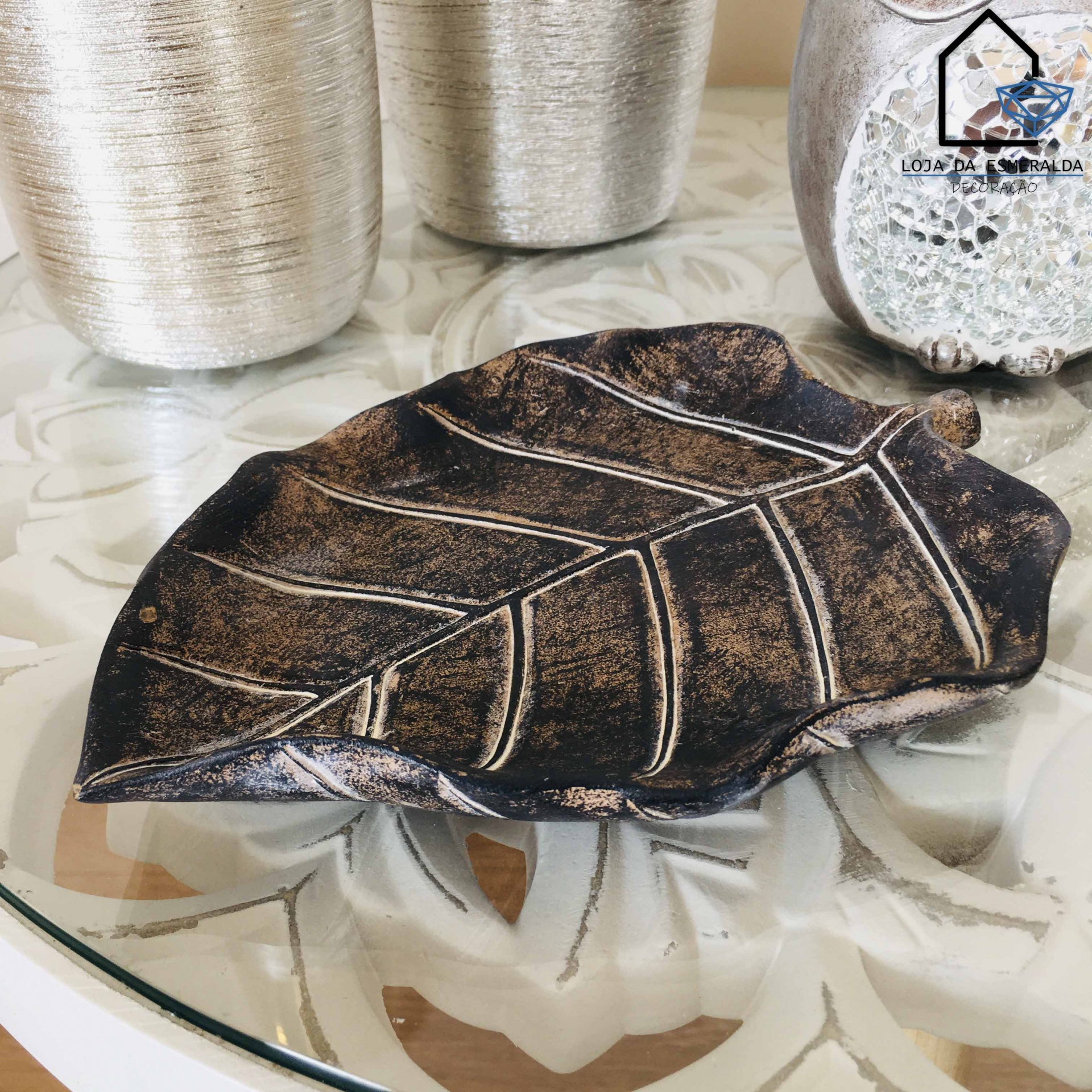 Prato decorativo em forma de folha em tons castanhos escuros sobre mesa de vidro