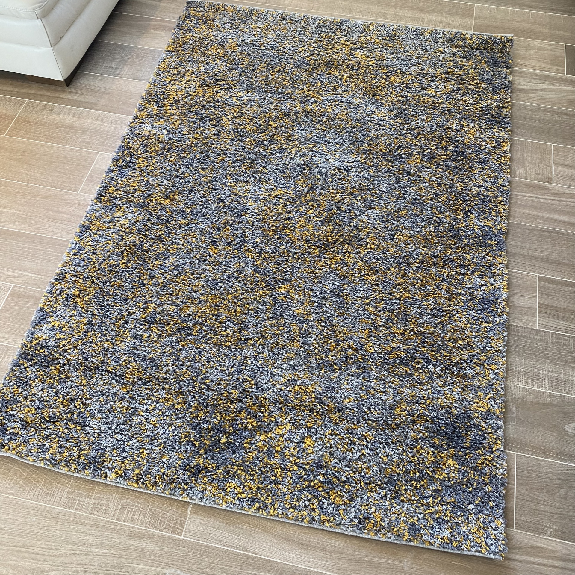 Tapete de pelo alto cinza e amarelo sobre chão de madeira com canto de sofá branco