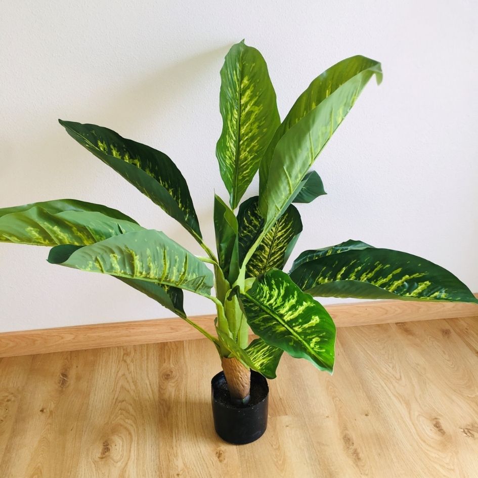 Planta artificial verde em vaso preto sobre chão de madeira