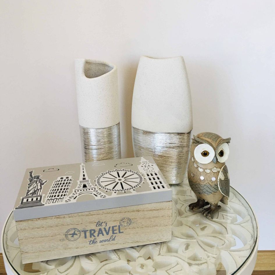 Caixa decorativa, dois vasos cerâmicos e estátua de coruja sobre mesa redonda de vidro.