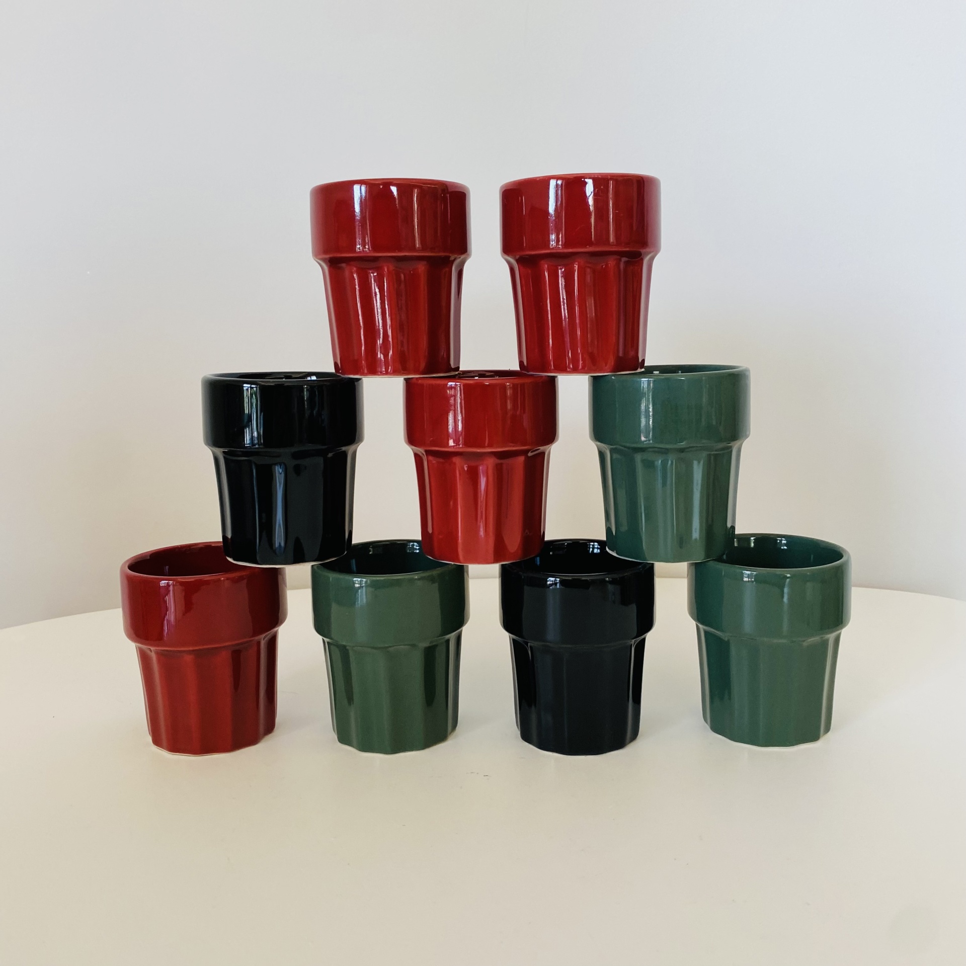 Dez vasos pequenos de cerâmica em vermelho, verde escuro e preto empilhados em pirâmide