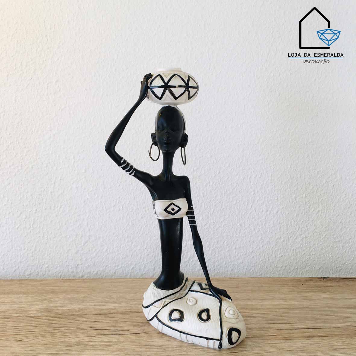 Estátua decorativa de mulher estilizada preto e branco com vaso na cabeça sobre superfície de madeira