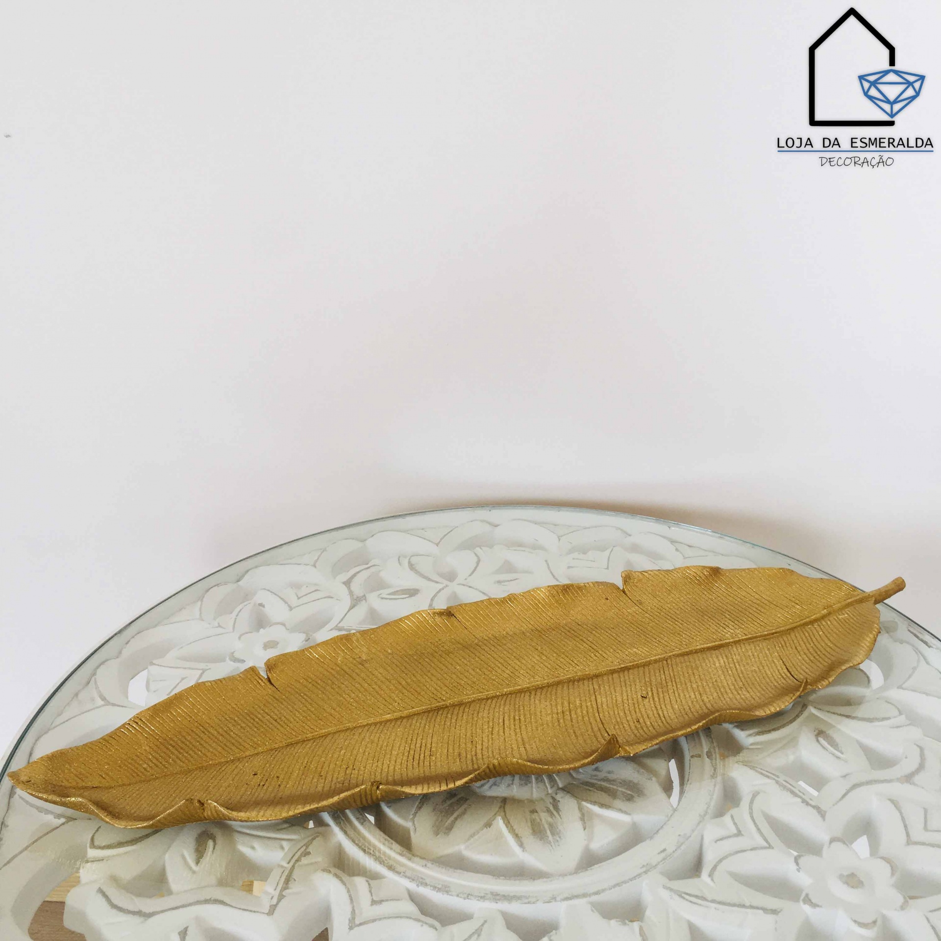 Prato decorativo dourado em forma de folha sobre superfície branca com padrão floral
