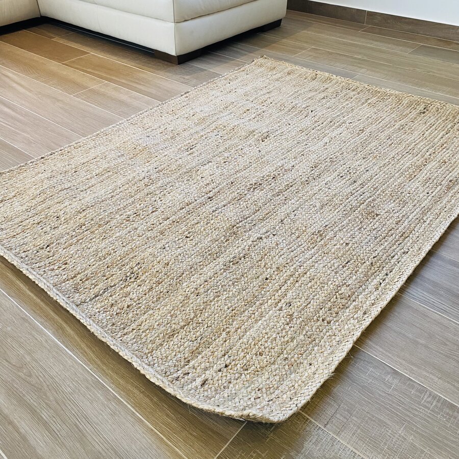 Tapete de tecido bege com textura trançada num chão de madeira clara, junto a um sofá branco