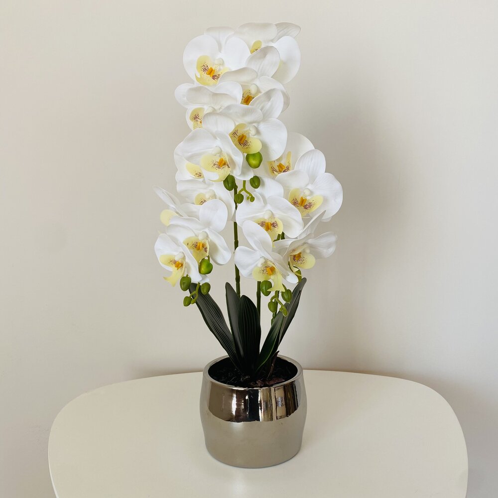 Orquídea artificial branca com vaso cinza em mesa branca