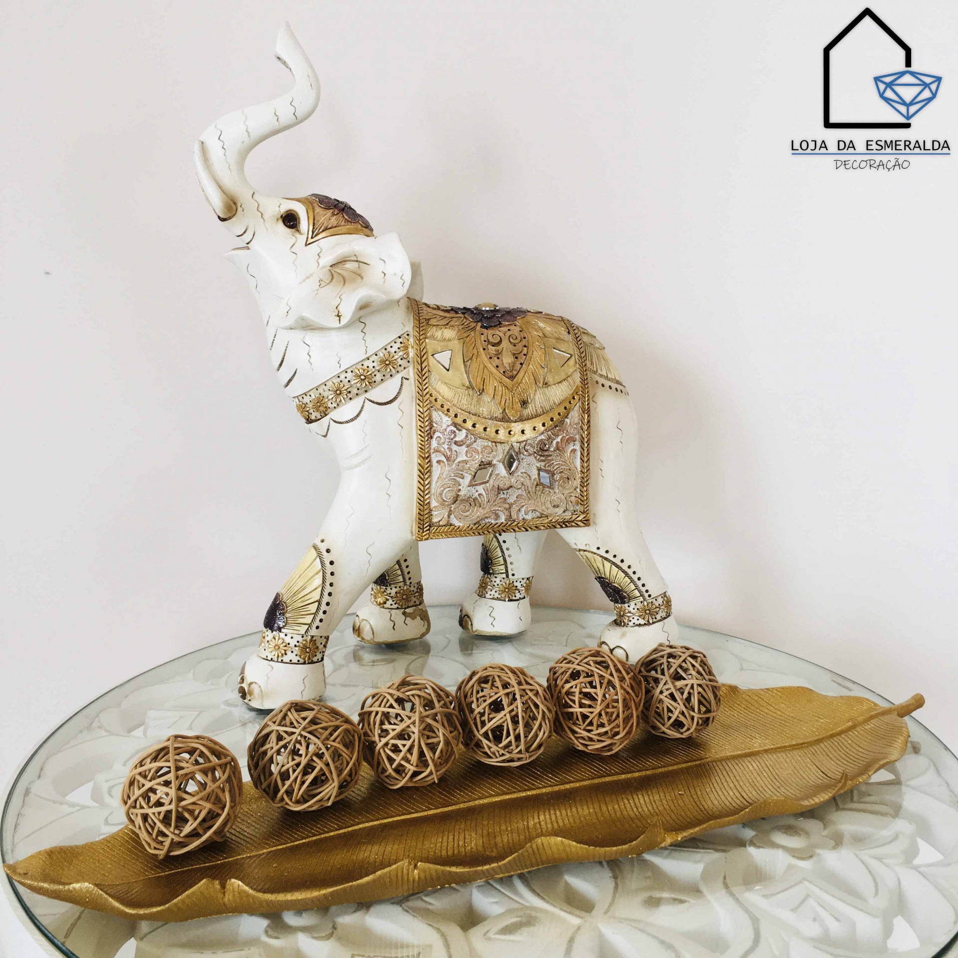 Figura decorativa de elefante branco com detalhes dourados e bolas de rattan numa bandeja dourada