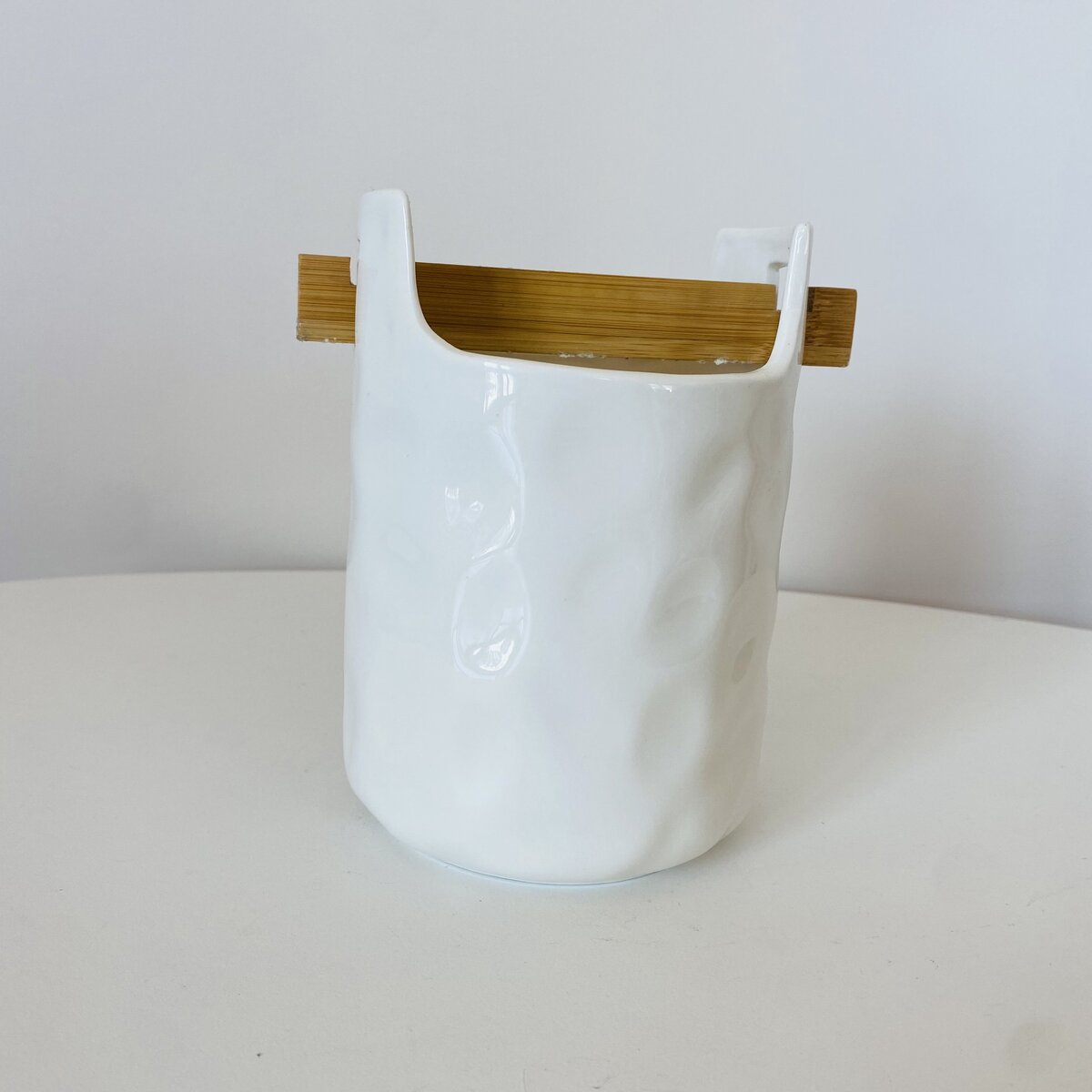 Vaso branco em cerâmica com tábua de madeira numa superfície branca