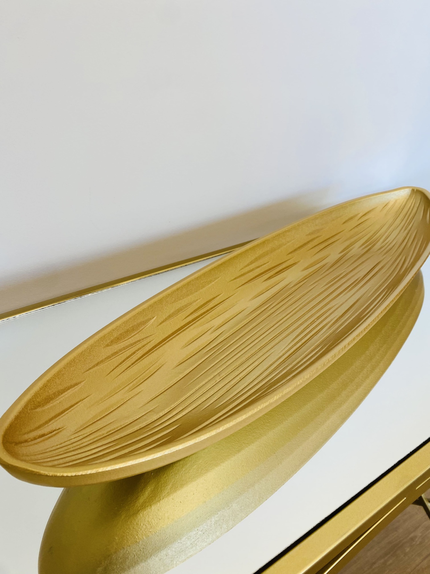 Fruteira oval dourada com textura riscada, em superfície espelhada