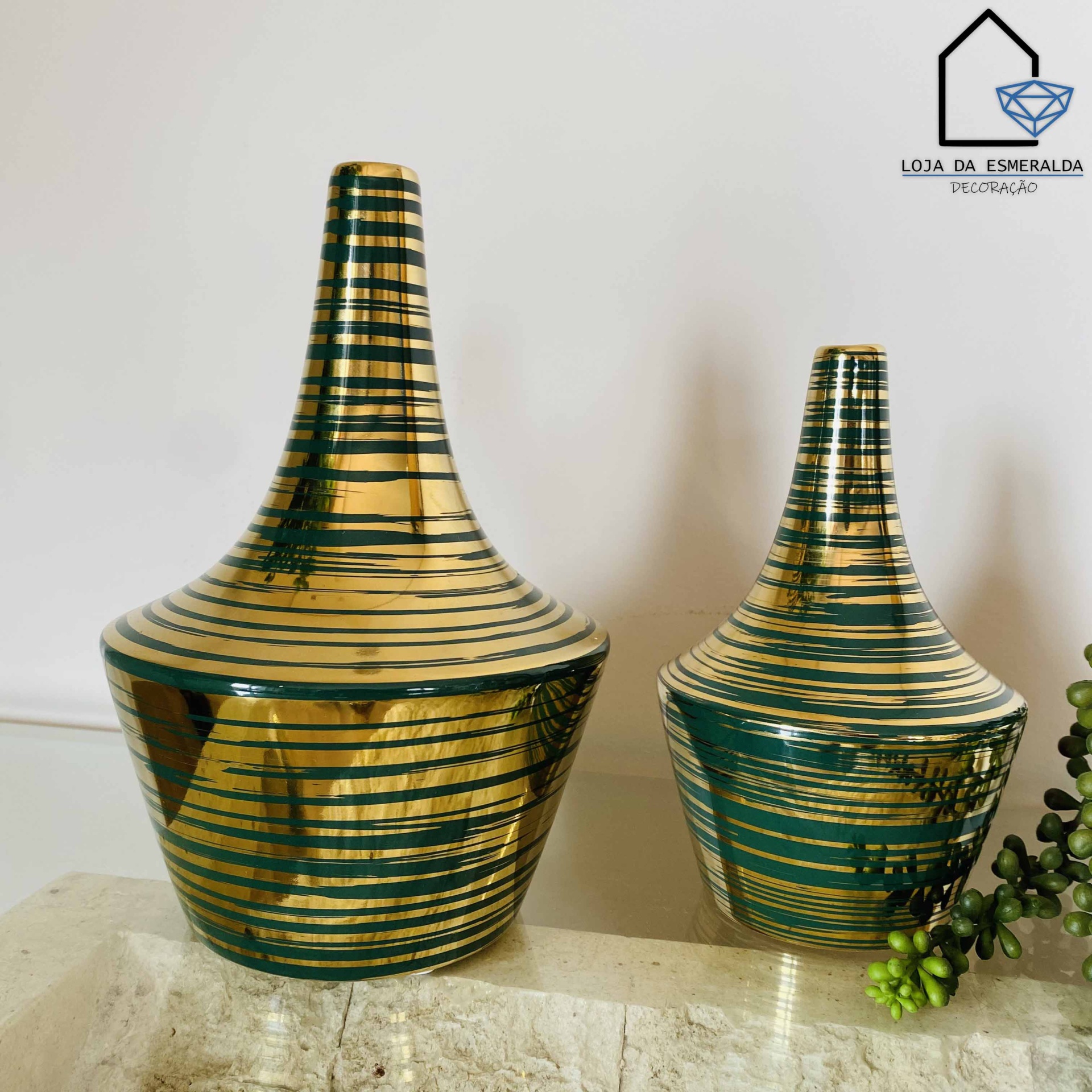Dois jarros decorativos dourados e verdes com listras sobre superfície de pedra
