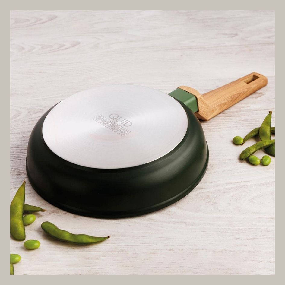 Frigideira preta com cabo de madeira claro e legumes verdes ao redor