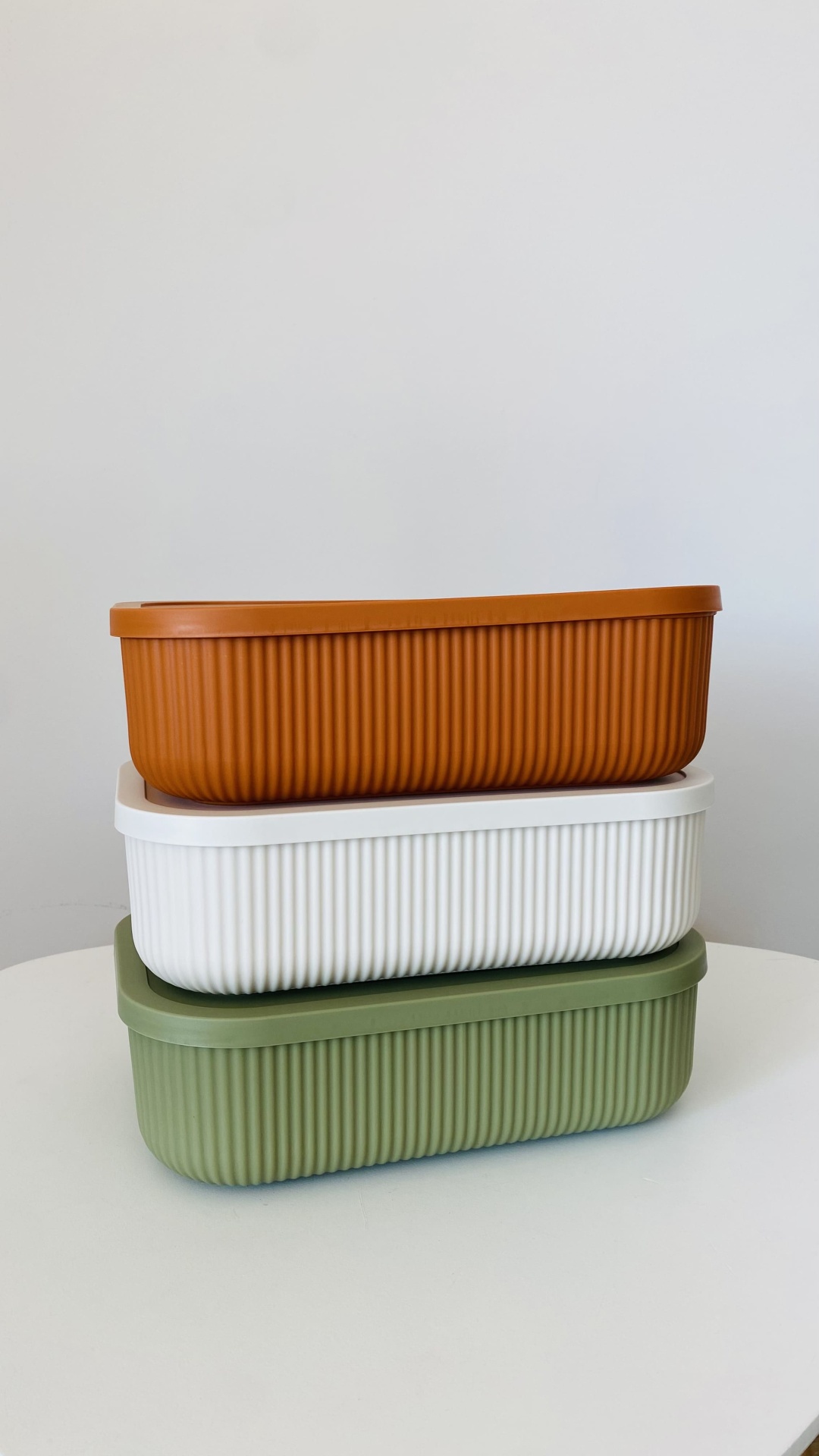 Três caixas retangulares de plástico nas cores castanho, branco e verde empilhadas.