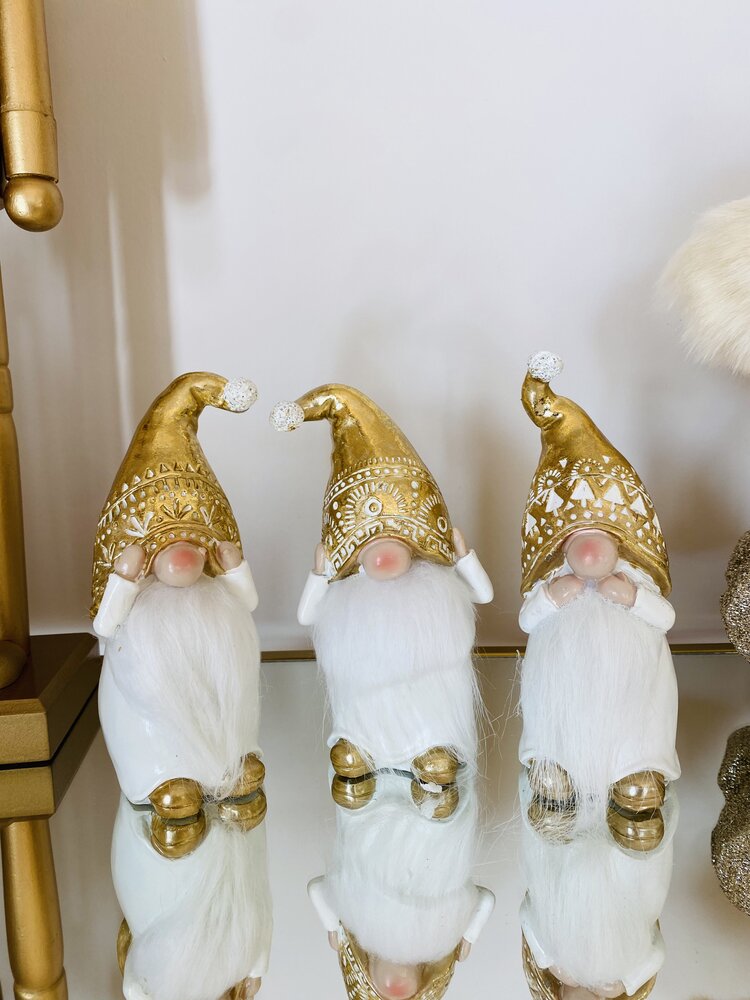 Três duendes decorativos com gorros dourados e barbas brancas em superfície espelhada.