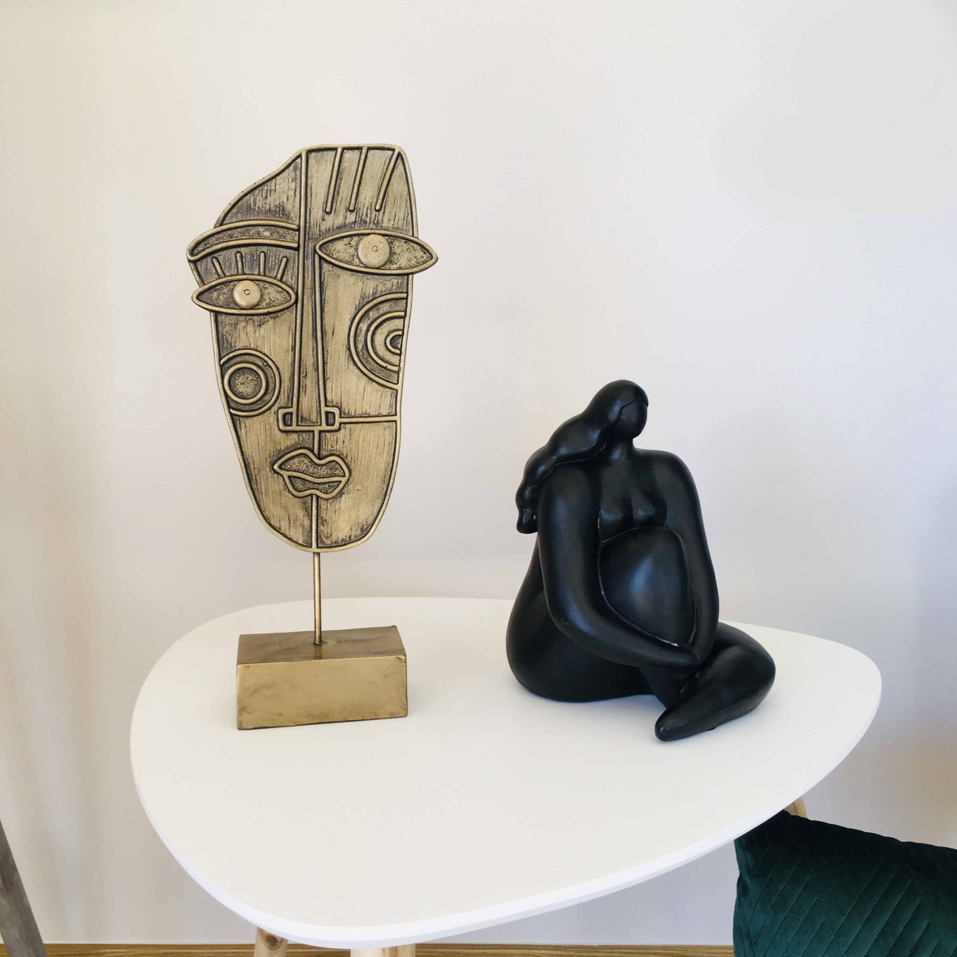 Mesa branca com duas esculturas decorativas, máscara dourada e escultura preta