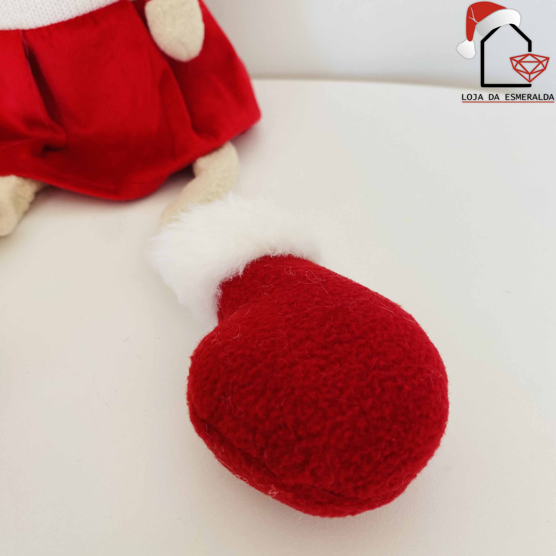 Luva vermelha felpuda com punho branco ao lado de boneco e logótipo Loja da Esmeralda