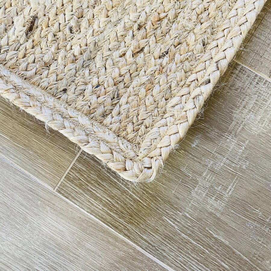 Canto de tapete bege trançado em fibra natural sobre chão de madeira clara