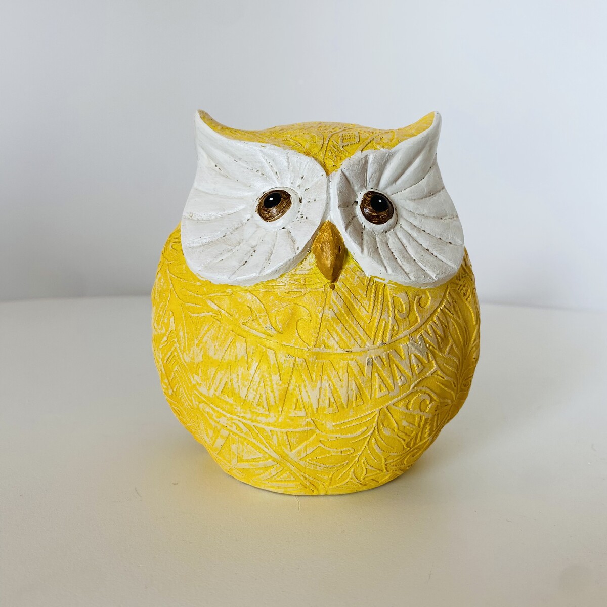 Figura decorativa de coruja amarela e branca com olhos castanhos.