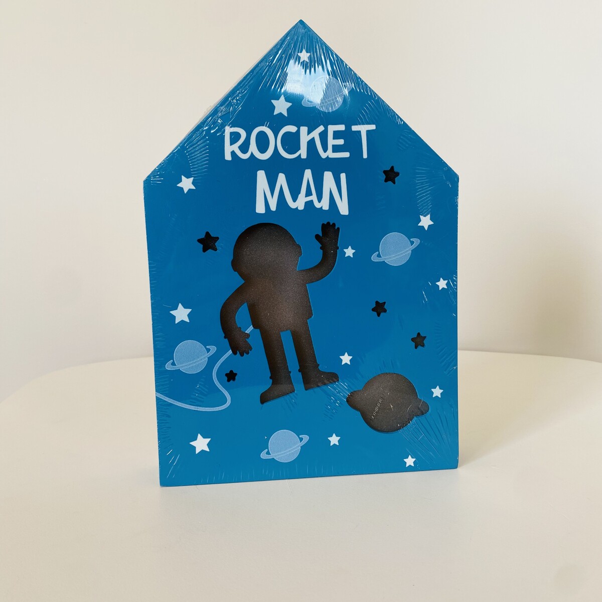Caixa azul em formato de casa com recorte de astronauta e texto ROCKET MAN