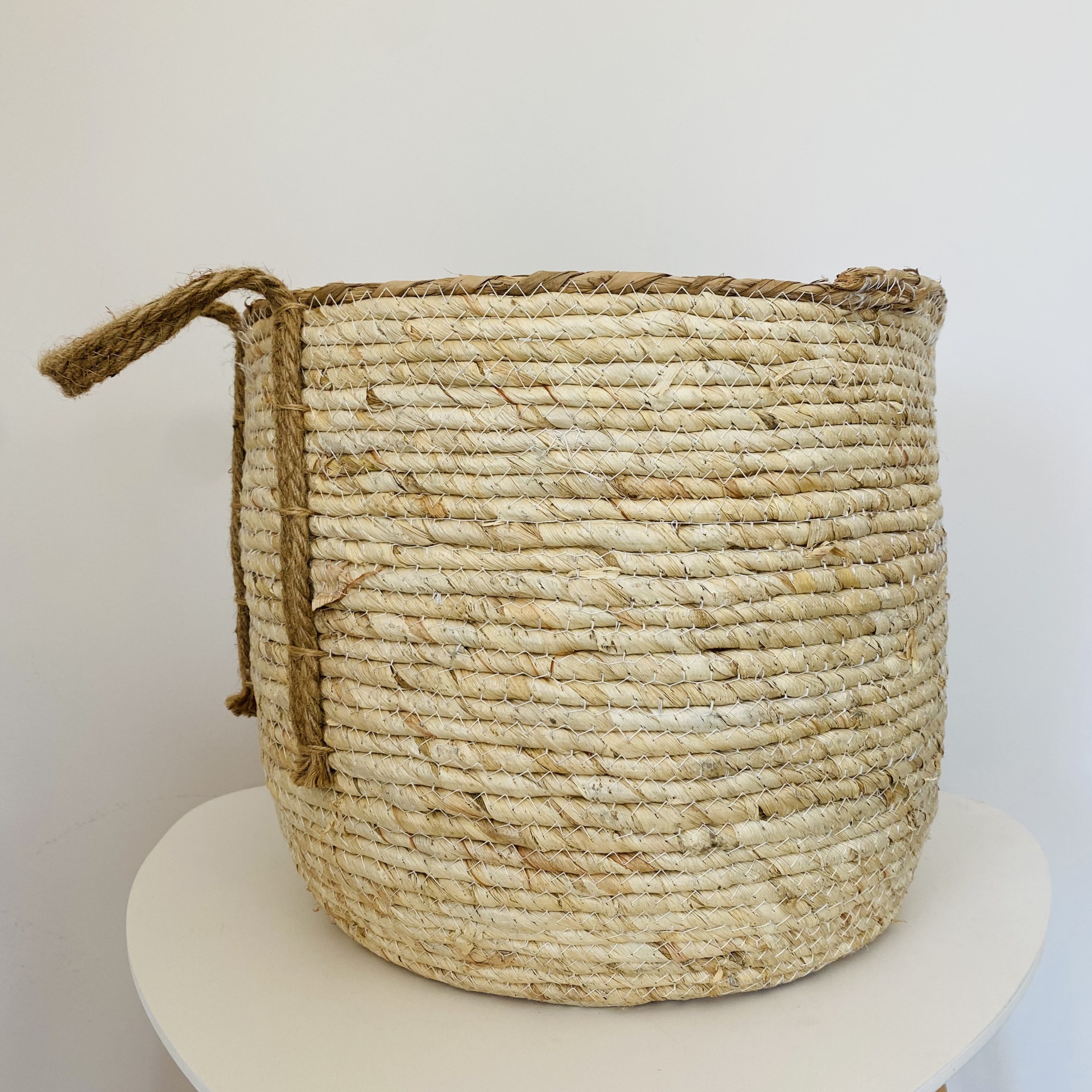 Cesto de fibra natural bege com alças num fundo branco