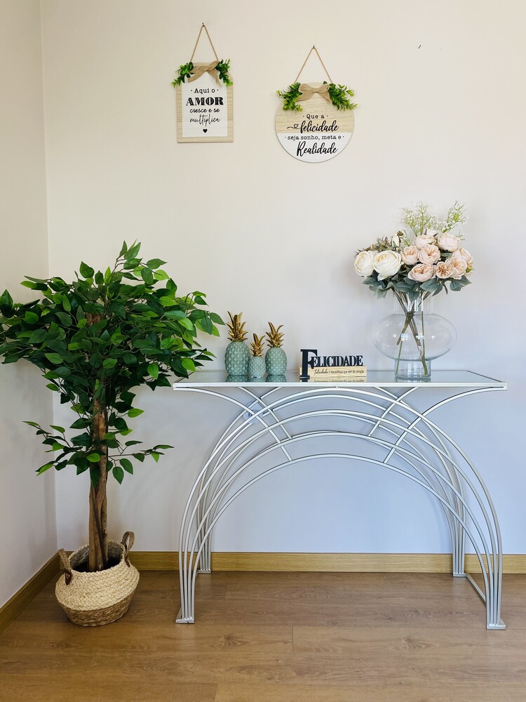 Consola metálica branca com tampo vidro com decoração e árvore artificial ao lado em vaso