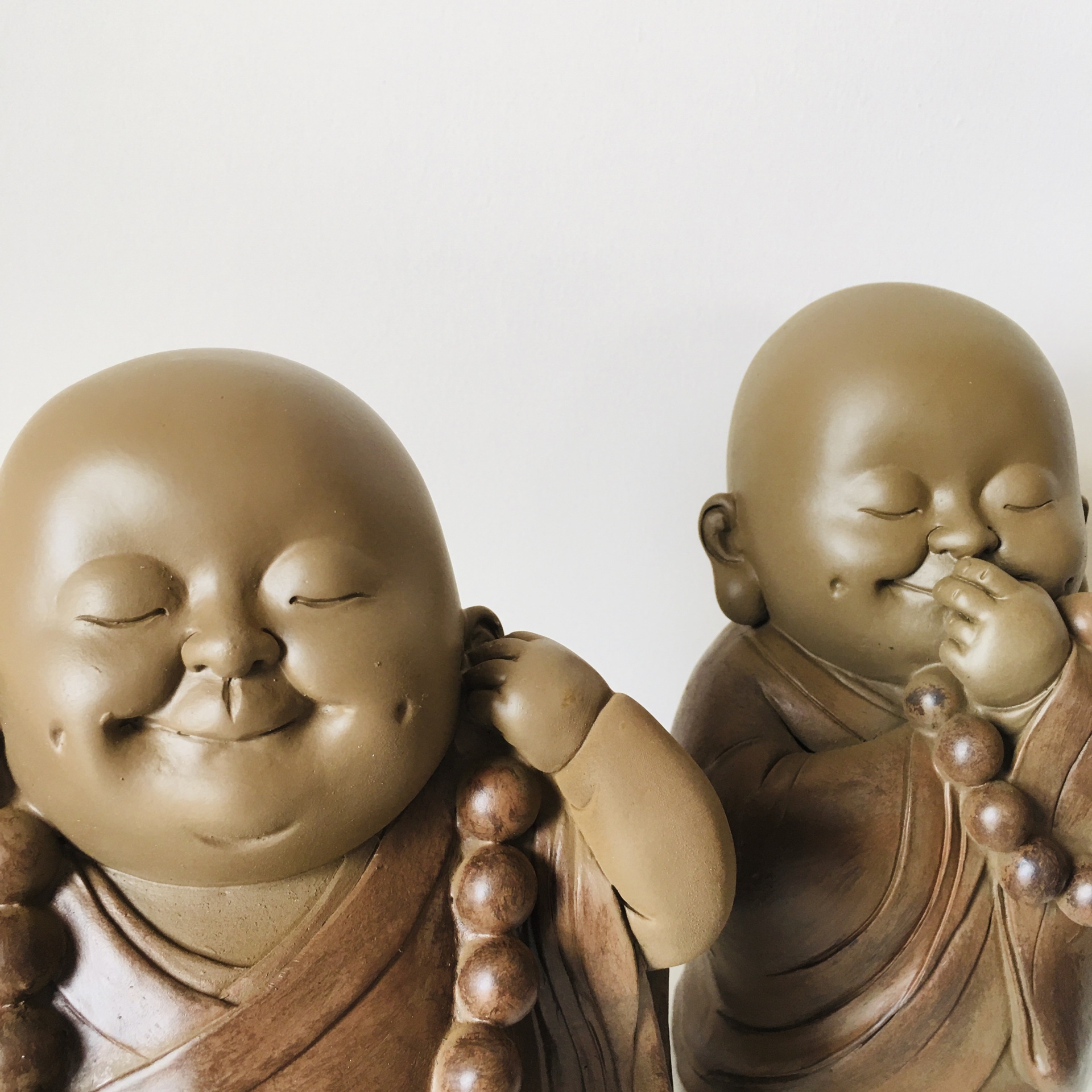 Estátuas de monges castanhos segurando colares de contas em fundo branco