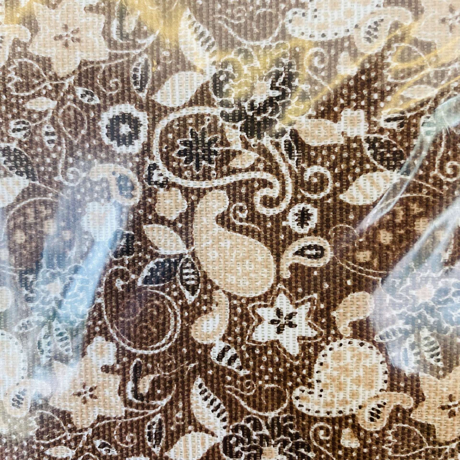 Tecido castanho com padrão floral e arabescos sob película plástica