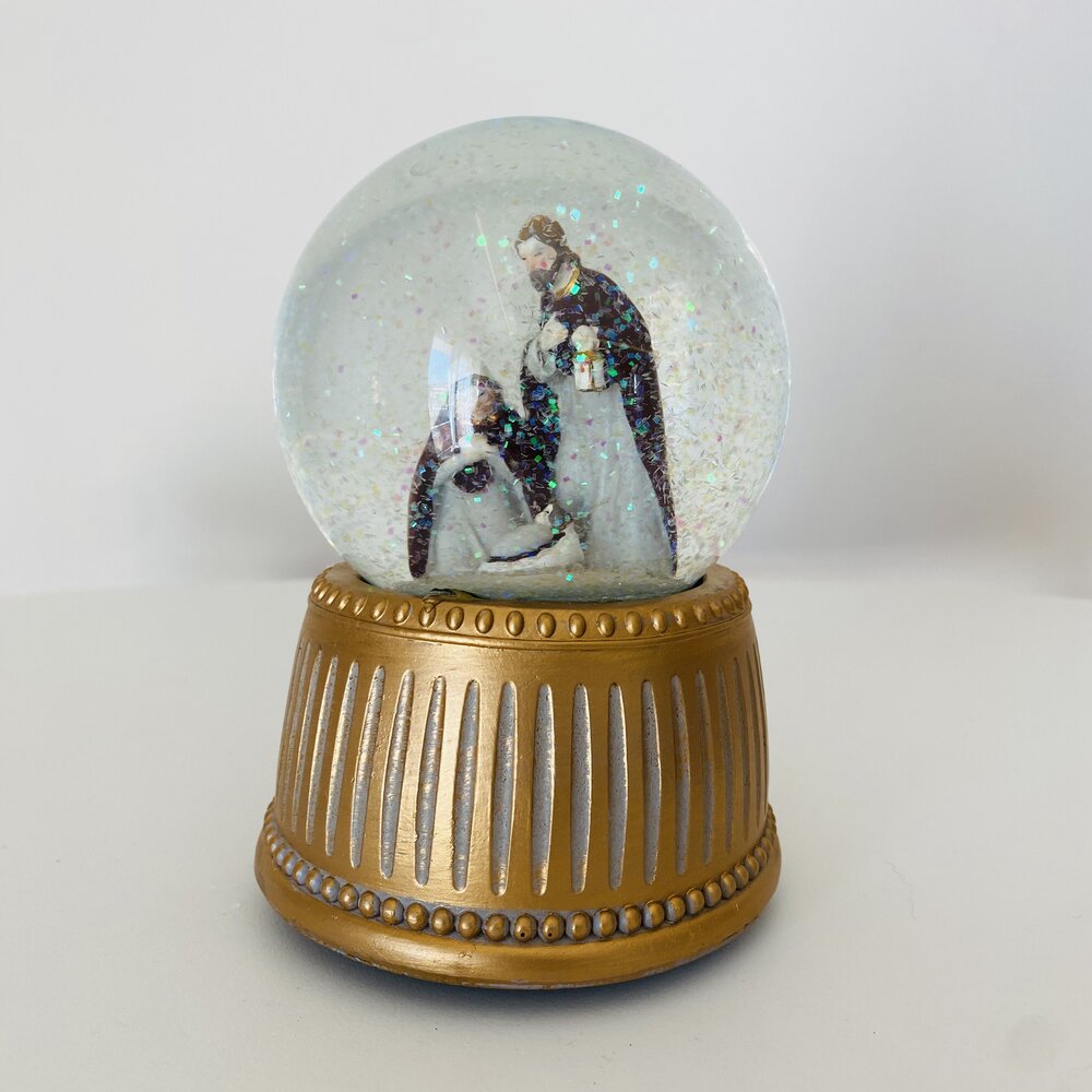 Globo de neve dourado com figuras religiosas e glitter prateado