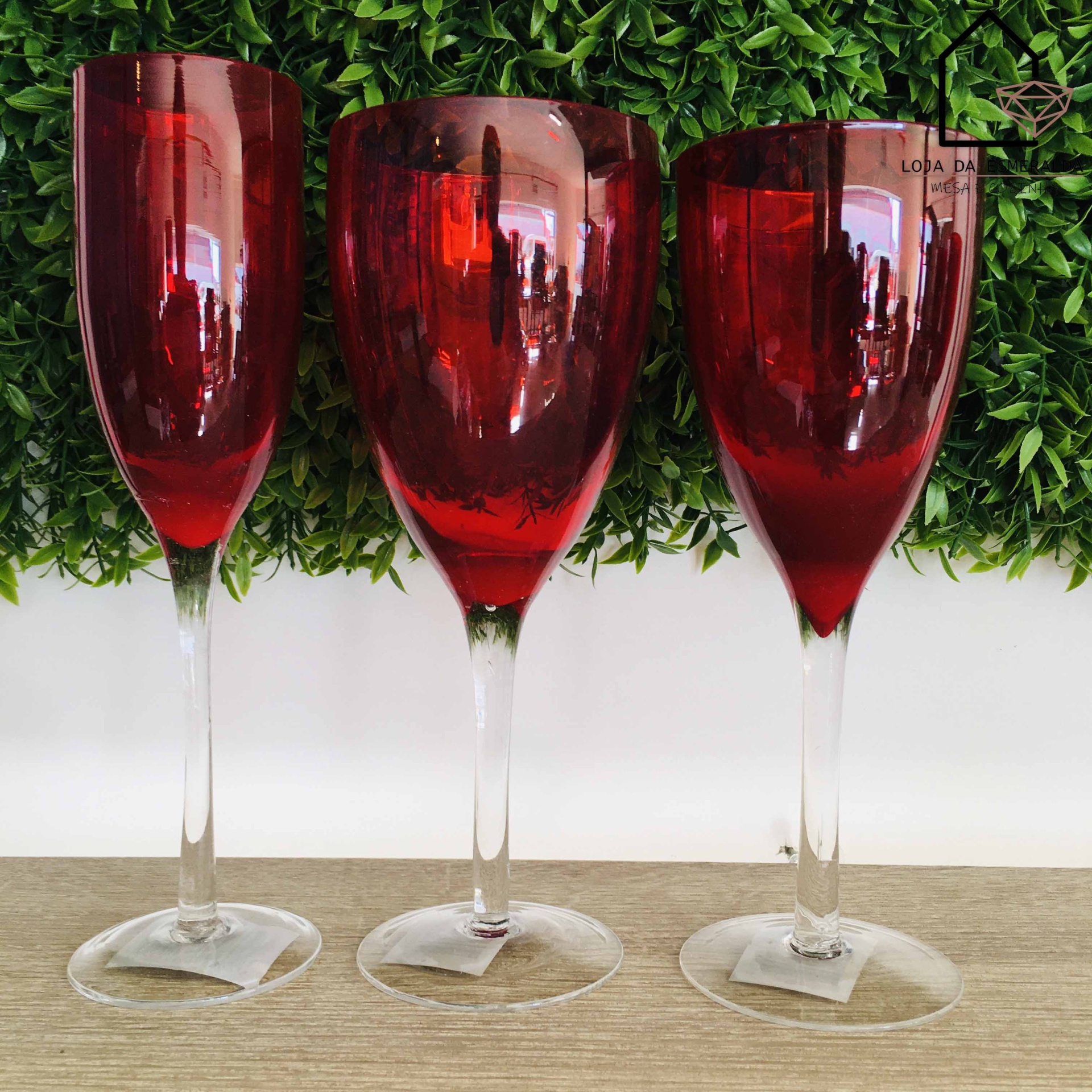 Três copos de vinho vermelhos com base transparente sobre mesa de madeira