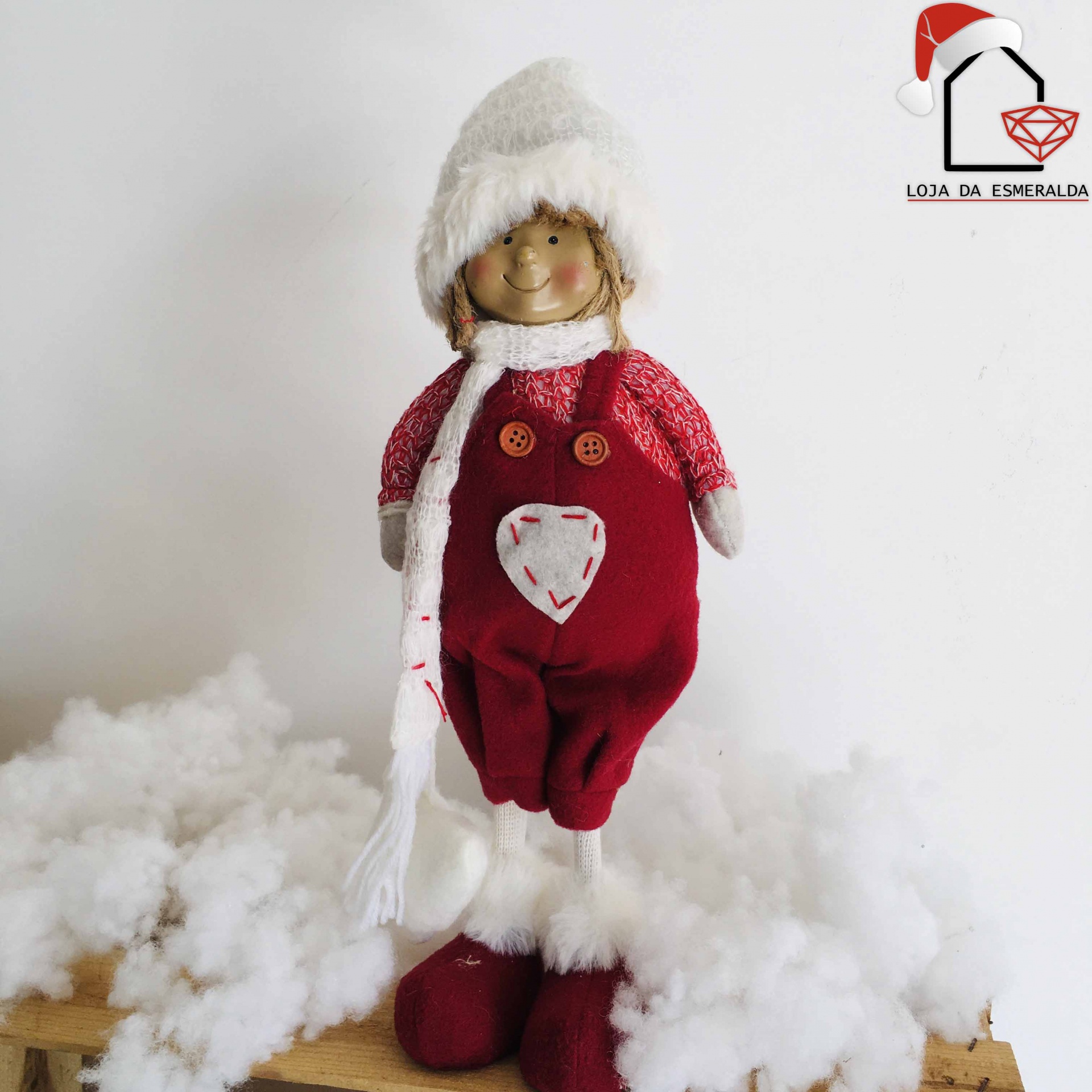 Boneco decorativo natalício com roupa vermelha e bege, chapéu e cachecol branco, botão castanho, sobre madeira e algodão branco