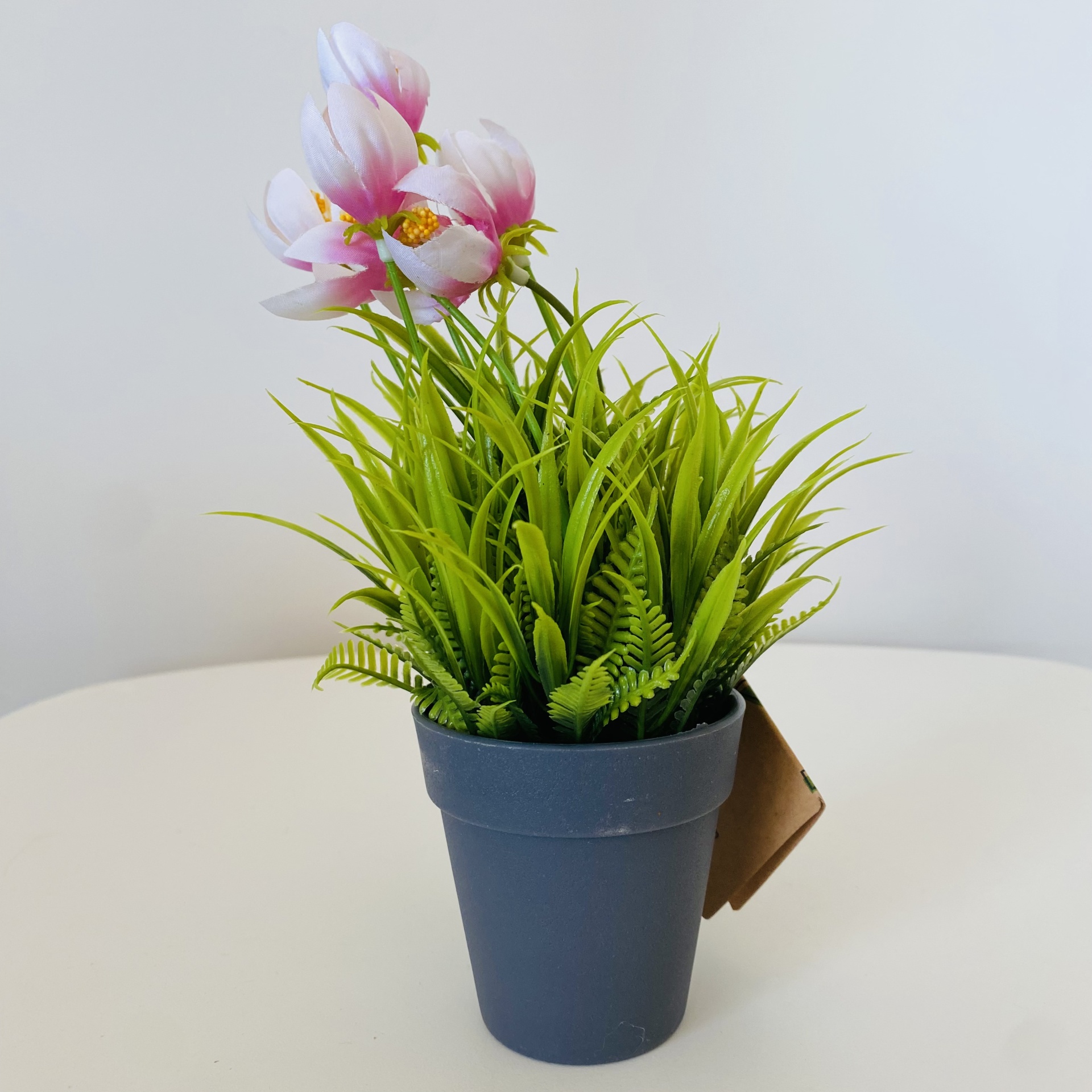 Vaso plástico cinzento com planta decorativa artificial verde e flores rosas brancas